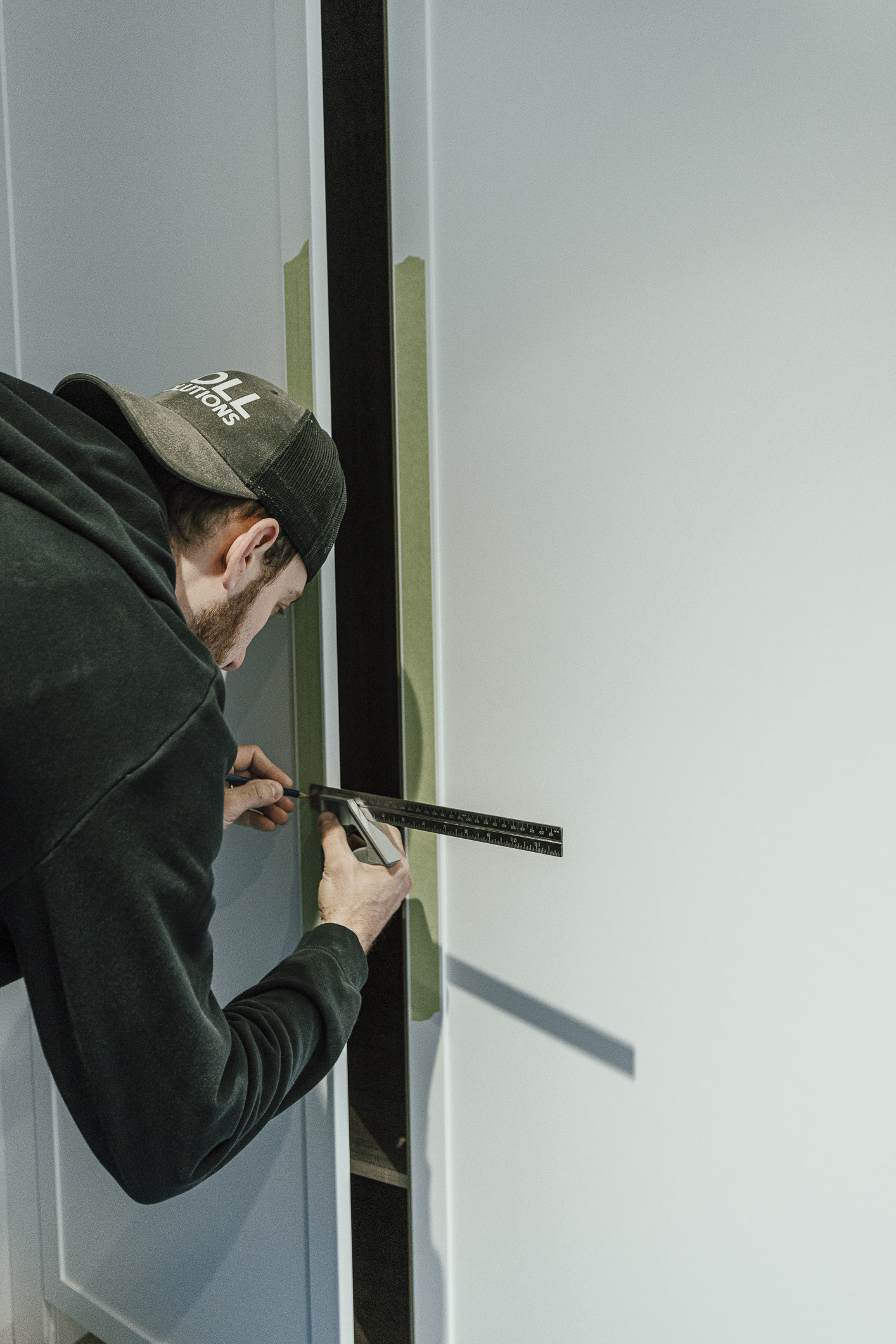 A focused individual measures a wall in a modern space, preparing for a DIY home improvement project.