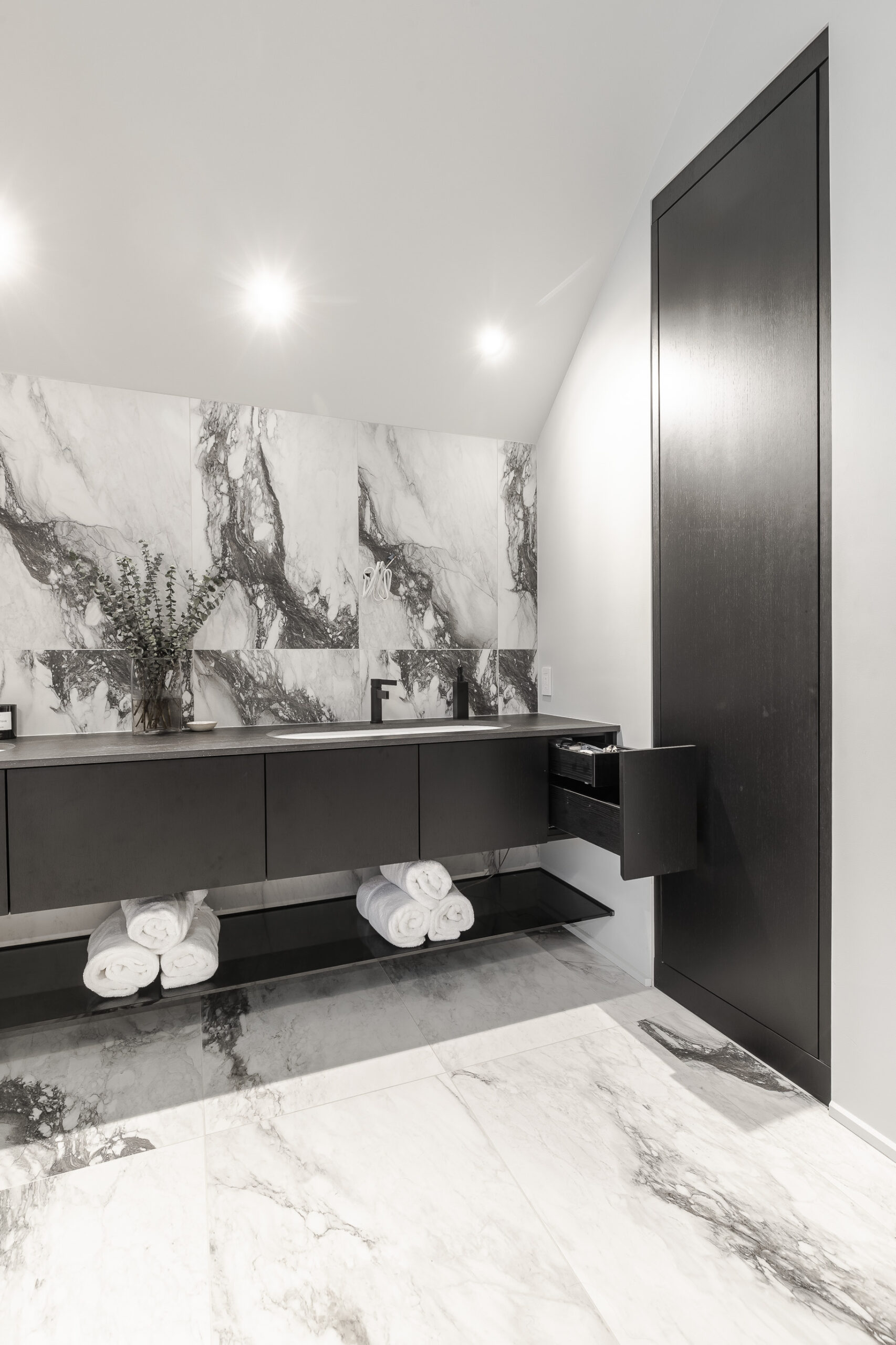 Discover a luxurious modern bathroom featuring elegant marble walls, a sleek black vanity, and minimalist decor for a tranquil retreat.