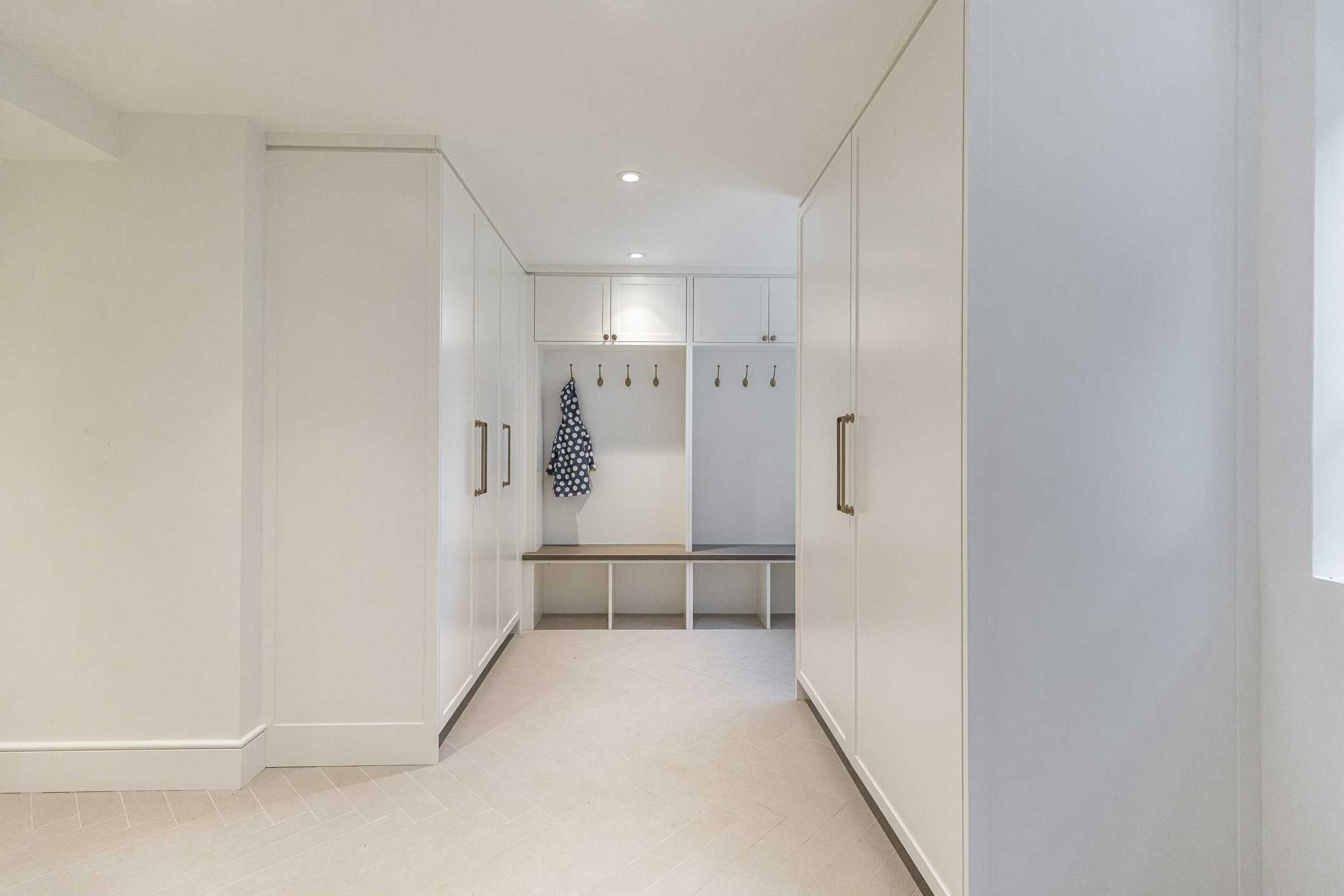 Discover a sleek modern entryway featuring white walls, stylish storage solutions, and a welcoming bench bathed in natural light.