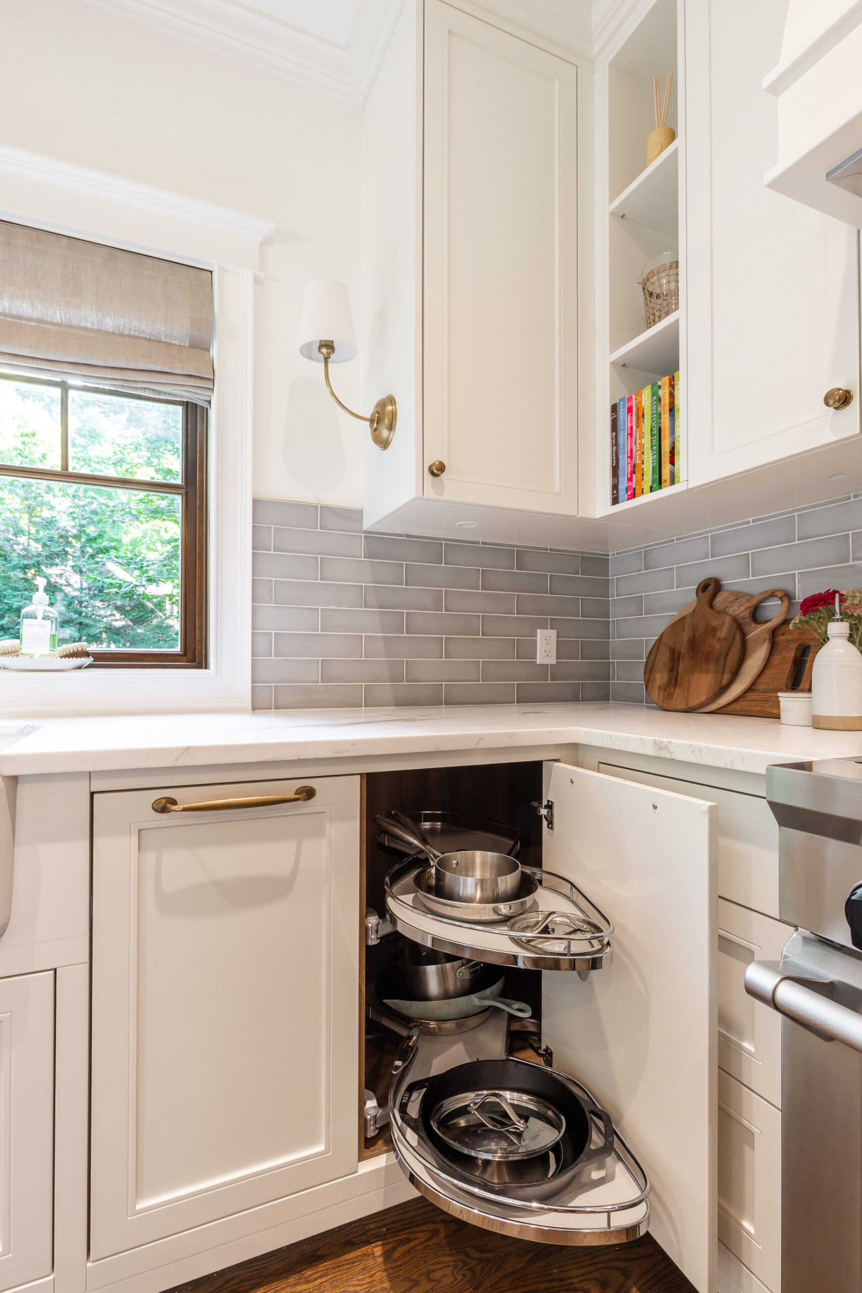 Elegant white kitchen featuring open shelves, a rotating corner cabinet, and abundant natural light, perfect for style and functionality.