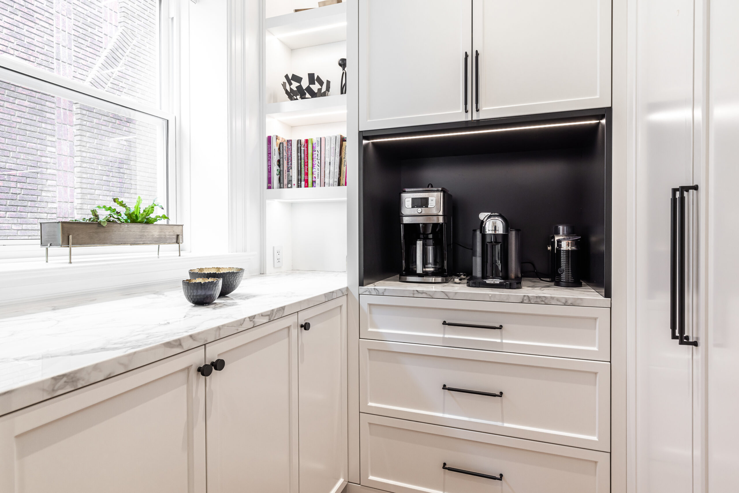 Stylish modern kitchen corner featuring sleek cabinetry, a bright marble countertop, and an organized coffee station bathed in natural light.