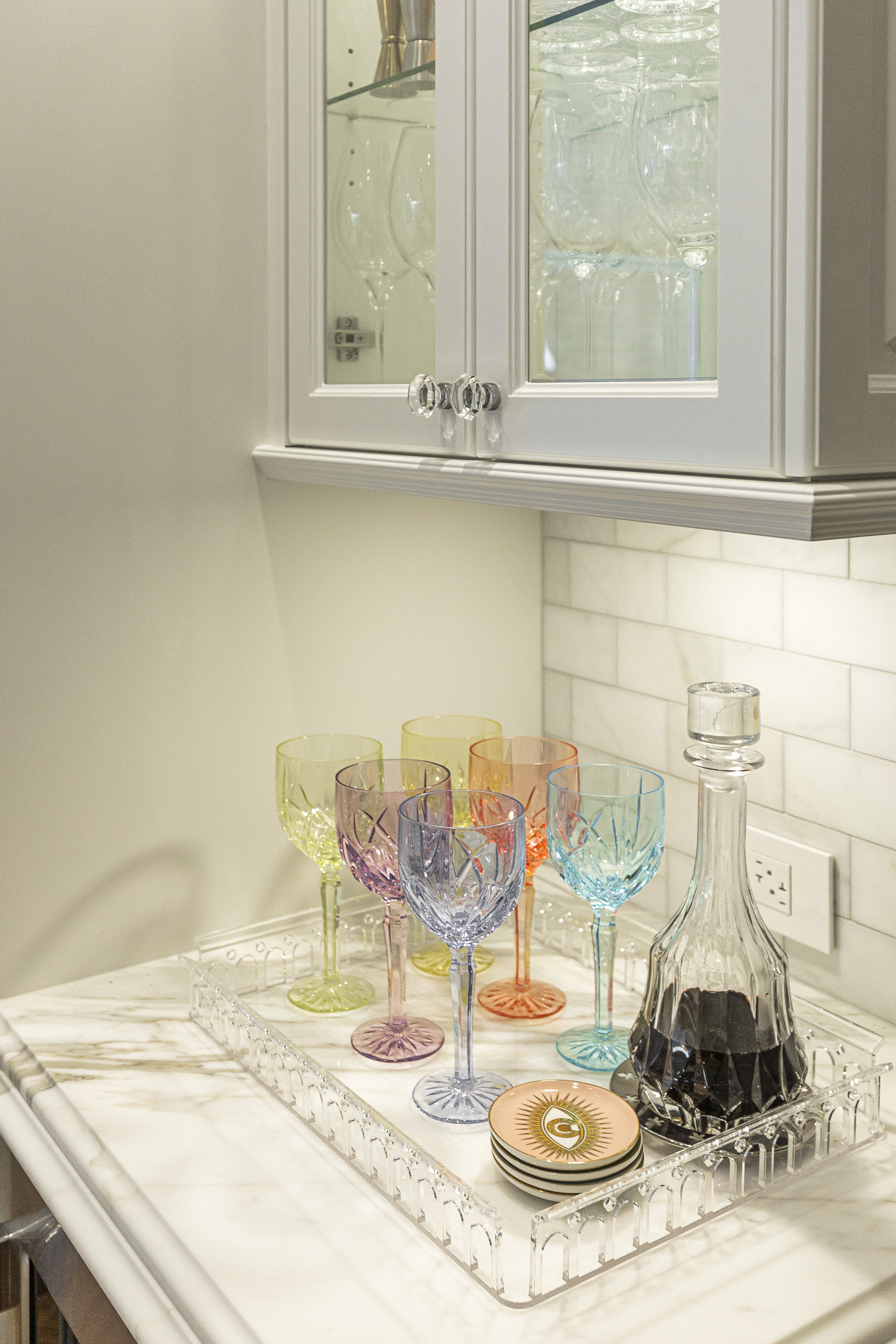 Colorful stemmed glasses and an elegant decanter create a sophisticated display in this chic kitchen bar area.