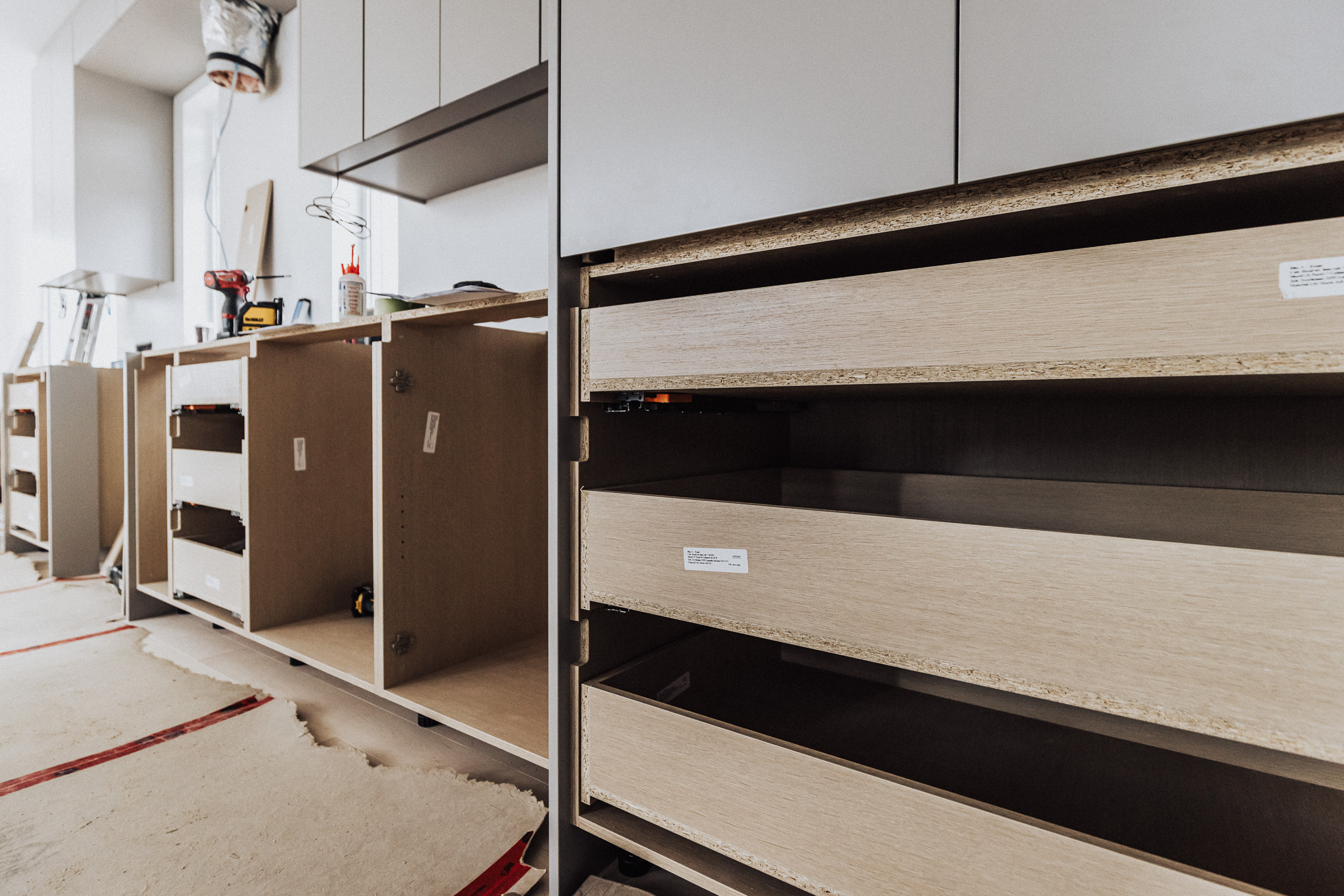 Modern kitchen renovation underway with light wood cabinets and organized open drawers, illuminated by bright natural light.