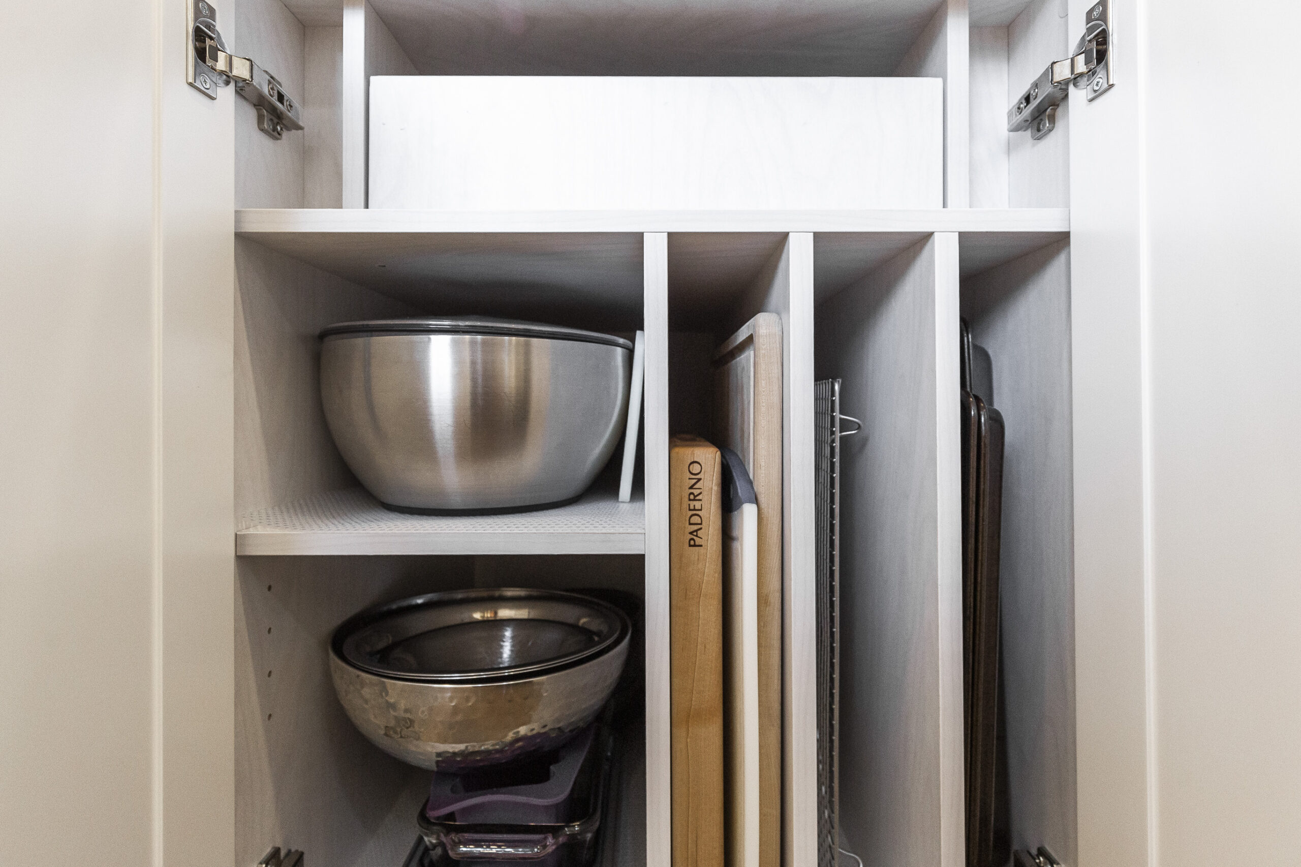 A modern kitchen cabinet features stainless steel bowls and neatly arranged cutting boards for efficient and stylish storage.