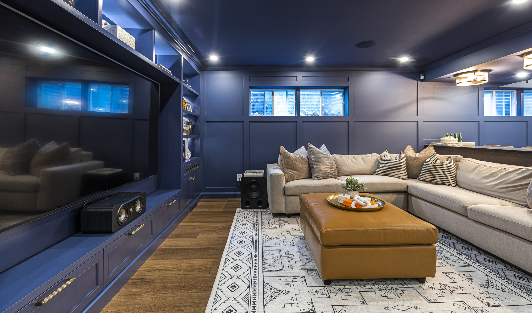 Cozy modern living room with blue walls, beige sectional, and burnt orange ottoman accents.