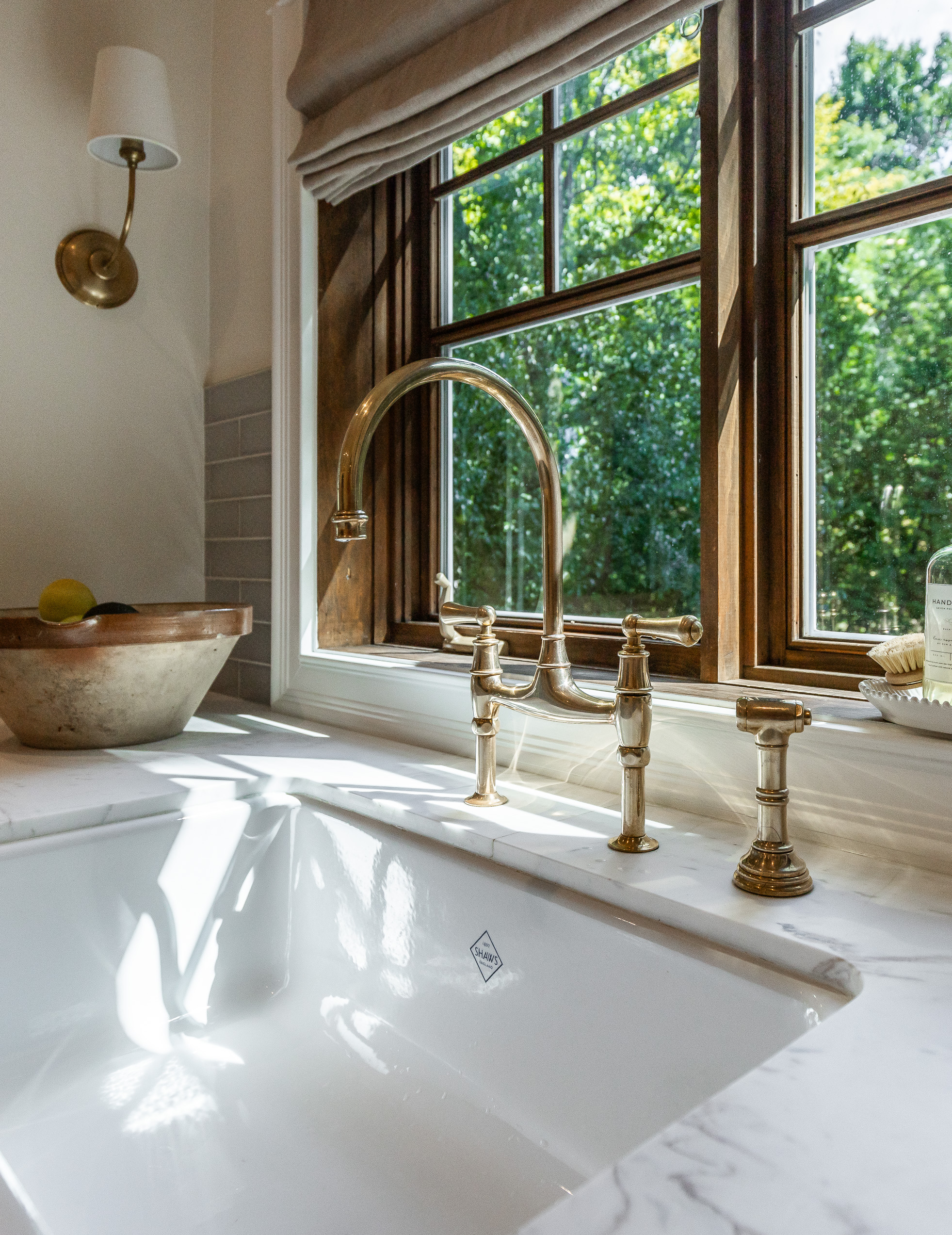 A luxurious marble sink with a brass faucet gleams in a serene bathroom, filled with natural light and elegant wooden accents.