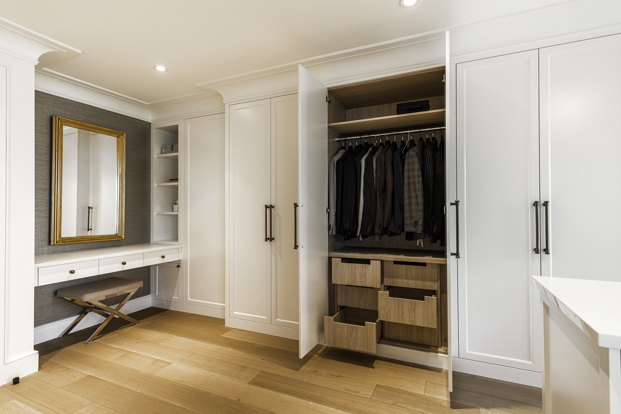 Experience organized luxury in this modern walk-in closet featuring sleek cabinetry, warm wood flooring, and elegant gold accents.