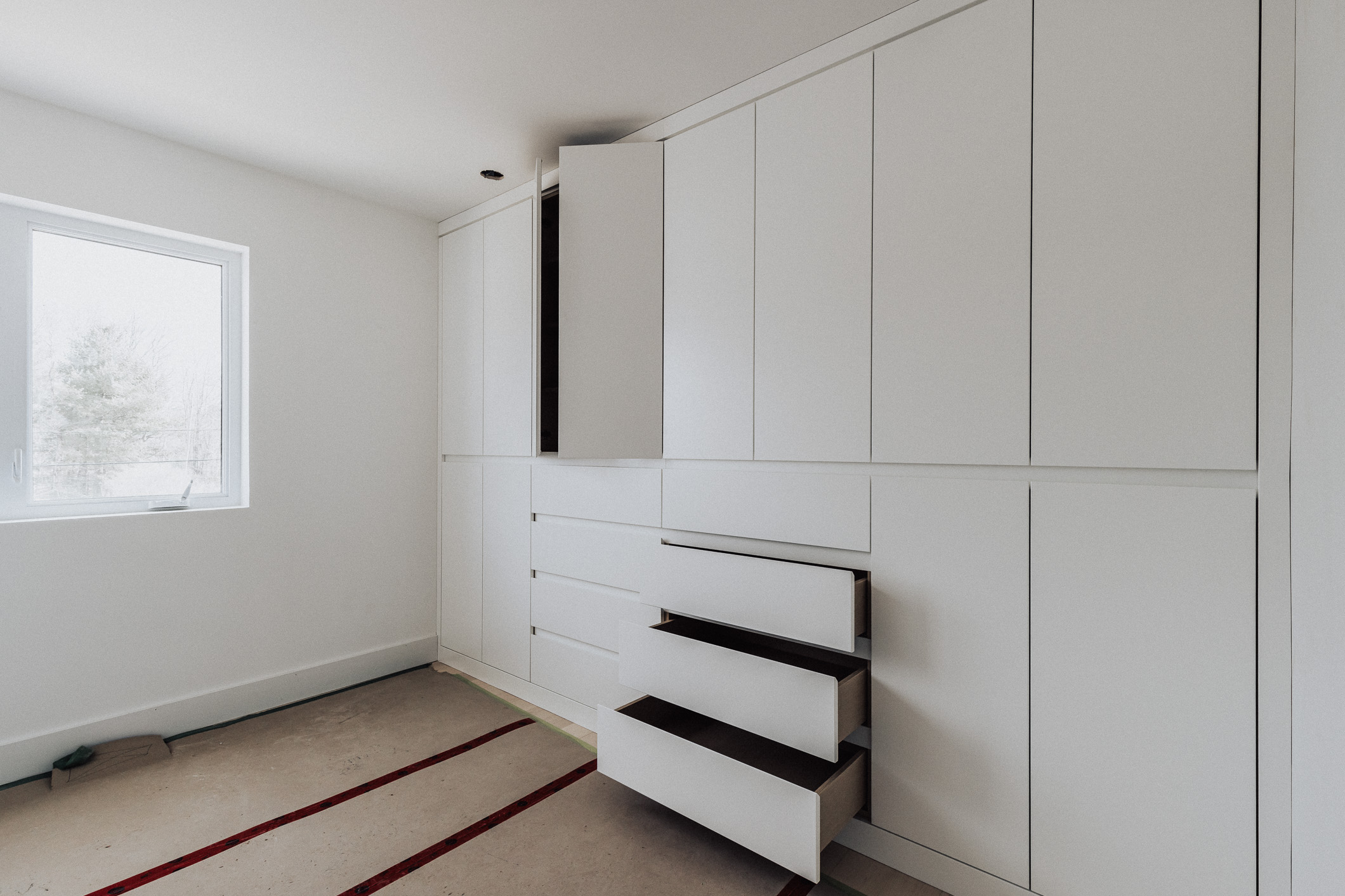 Bright minimalist room with white cabinetry, large window, and subtle beige carpet detailing.