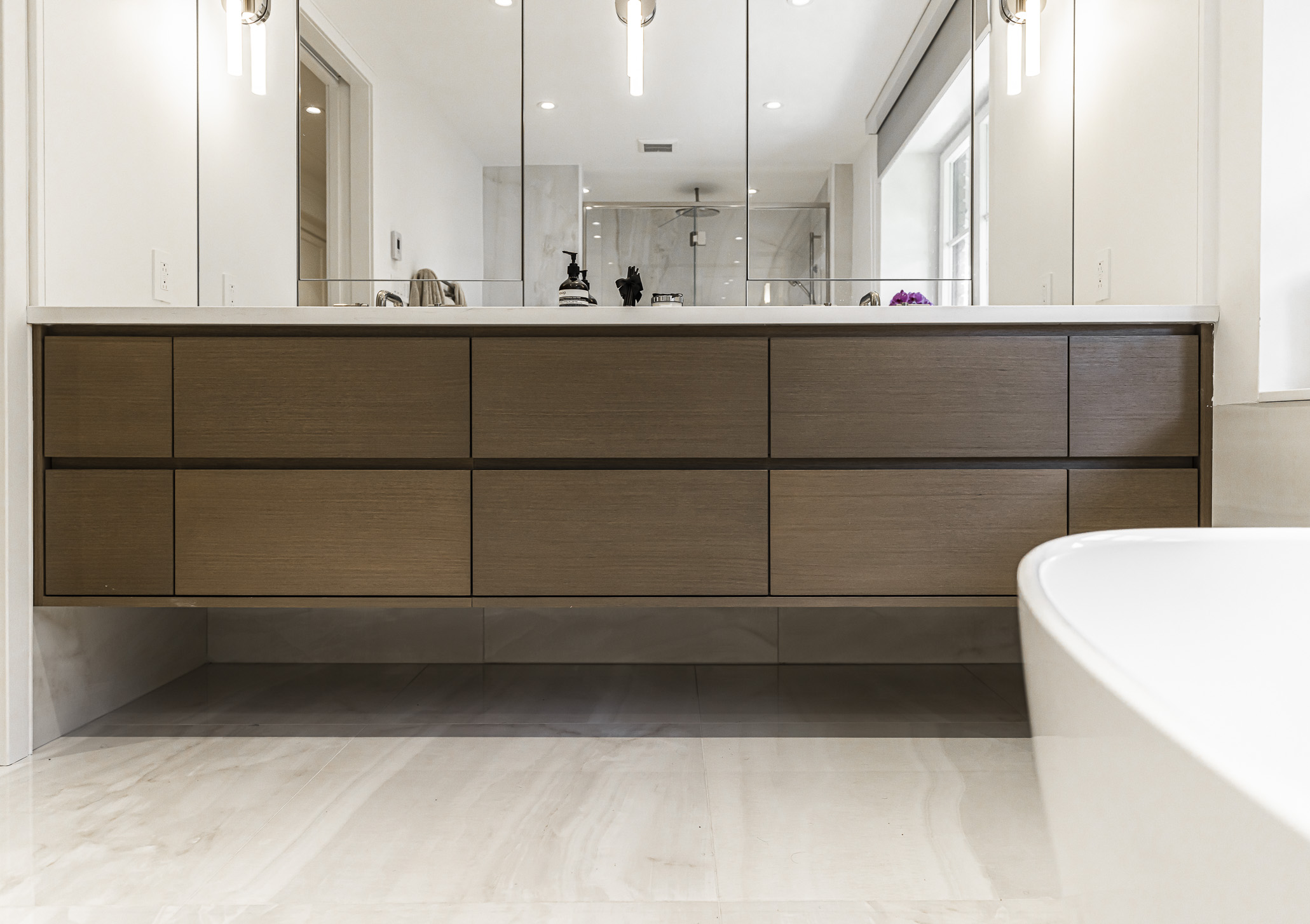 Discover a serene modern bathroom featuring a dark wood vanity, expansive mirrors, and a stylish freestanding bathtub for ultimate relaxation.