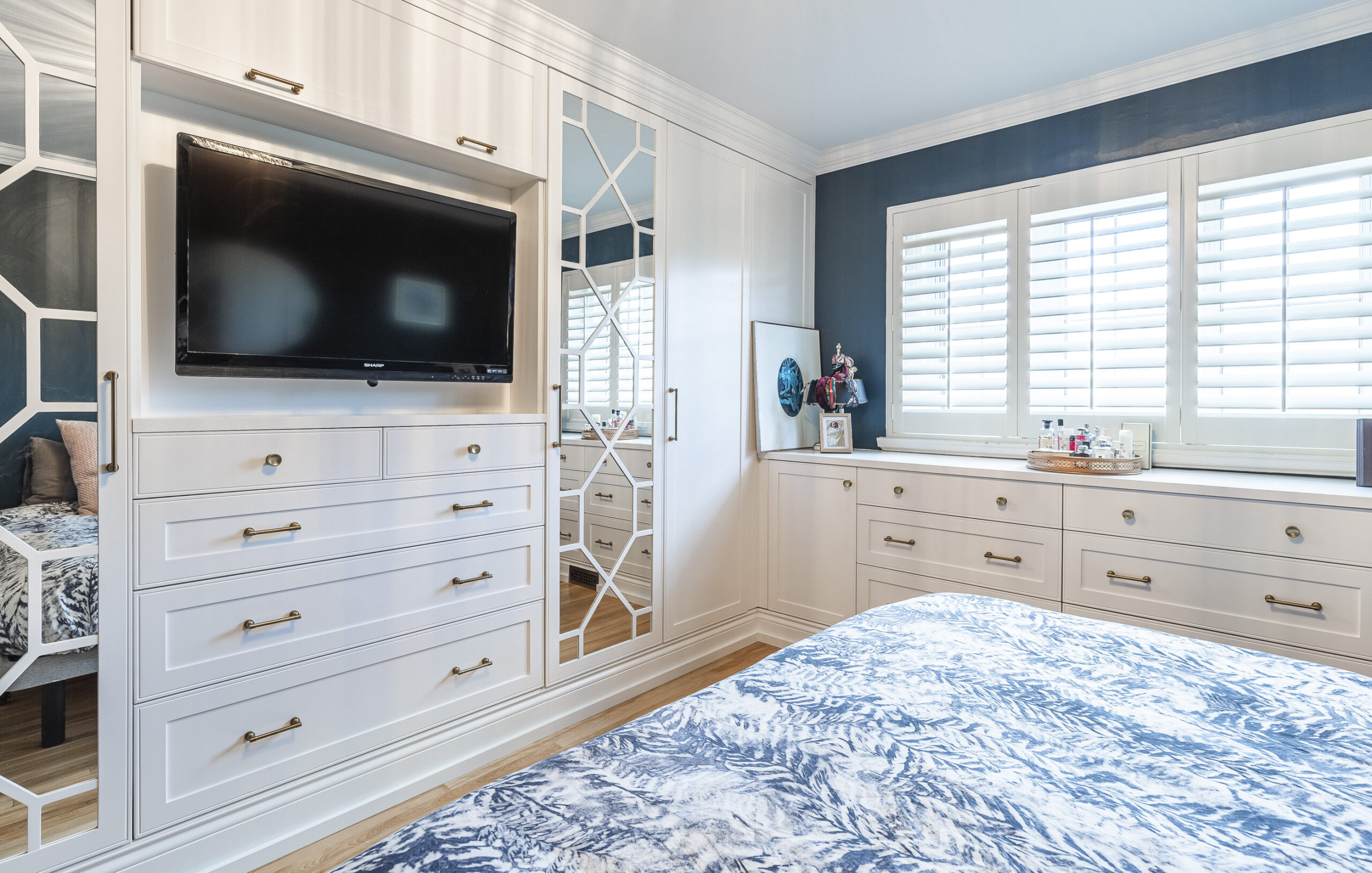 Experience tranquility in this modern bedroom featuring a stylish blue and white bedspread, sleek white furniture, and abundant natural light.