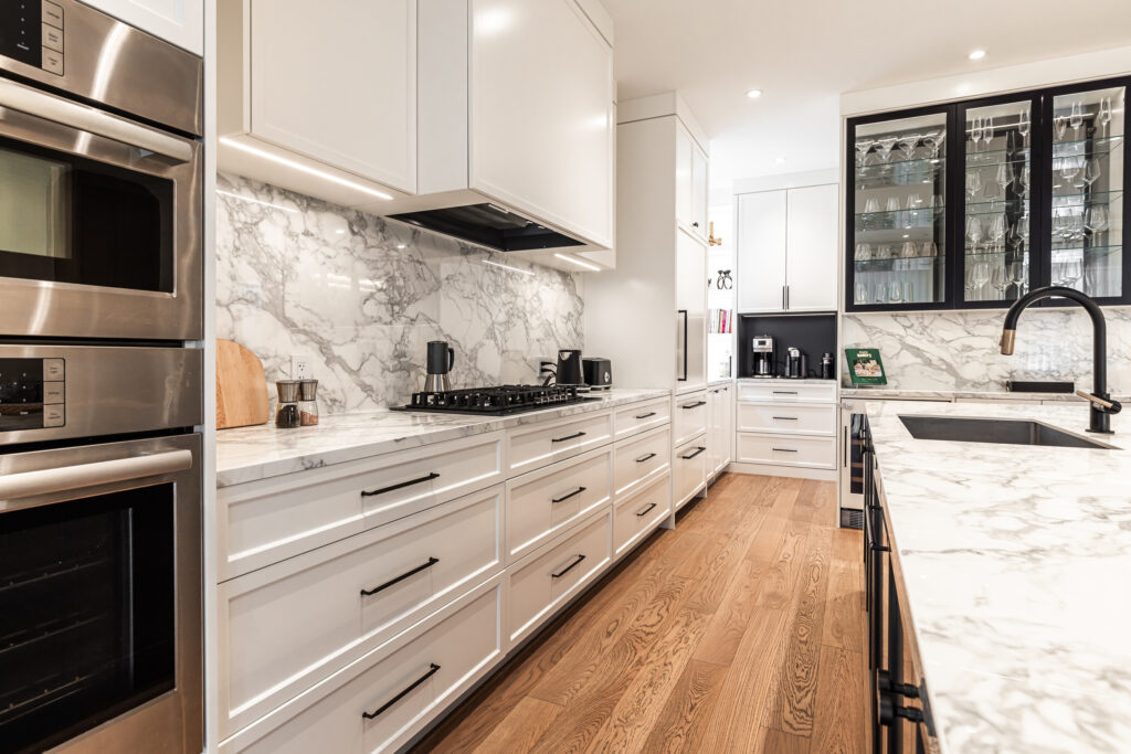 Sleek white kitchen with marble backsplash, stainless steel appliances, and natural light.