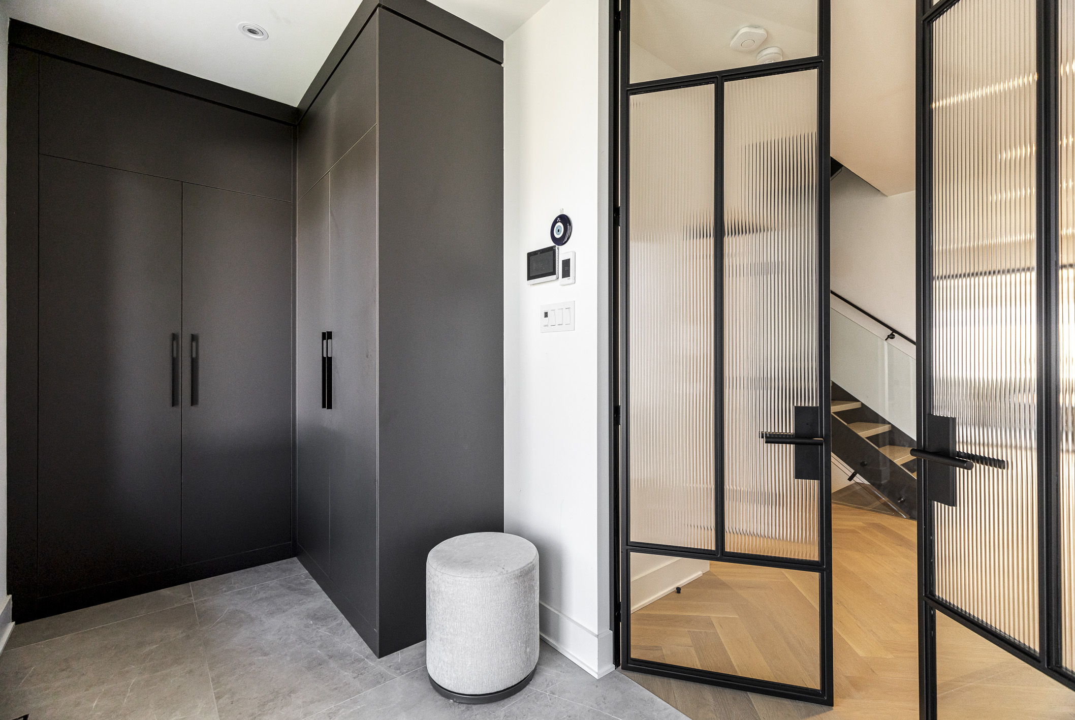 Modern entryway featuring a sleek black closet, a light round stool, and airy glass doors that invite natural light.