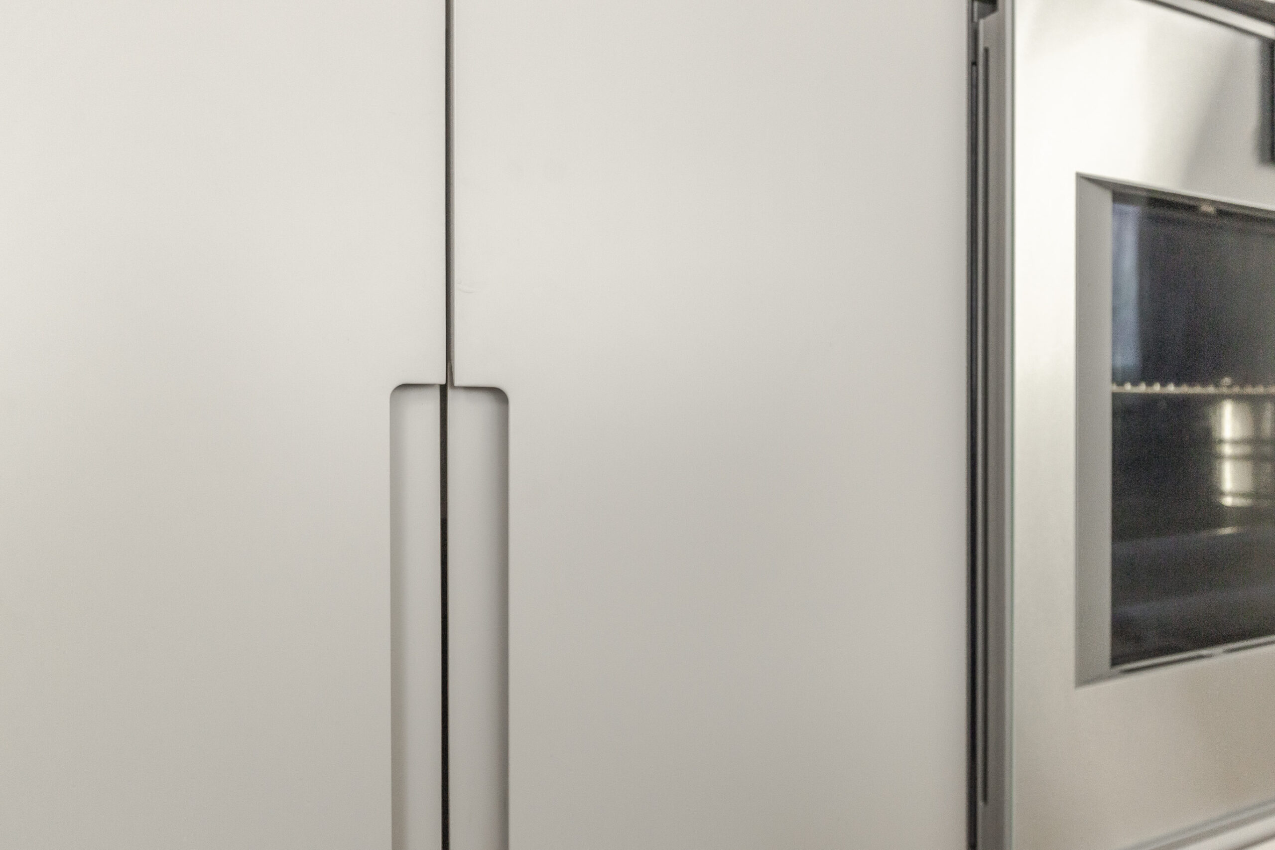A modern white refrigerator with elegant handles and an integrated oven enhances the sleek design of this contemporary kitchen.