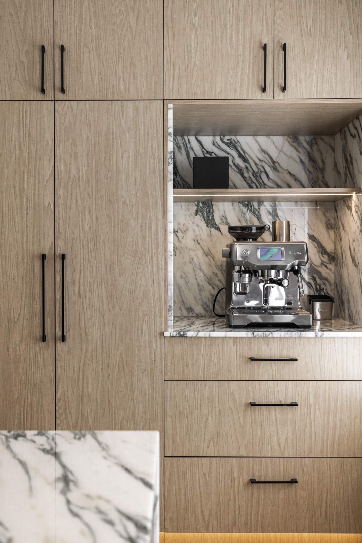 Modern kitchen design features light wood cabinetry, an elegant coffee station with marble accents, and a stylish espresso machine.
