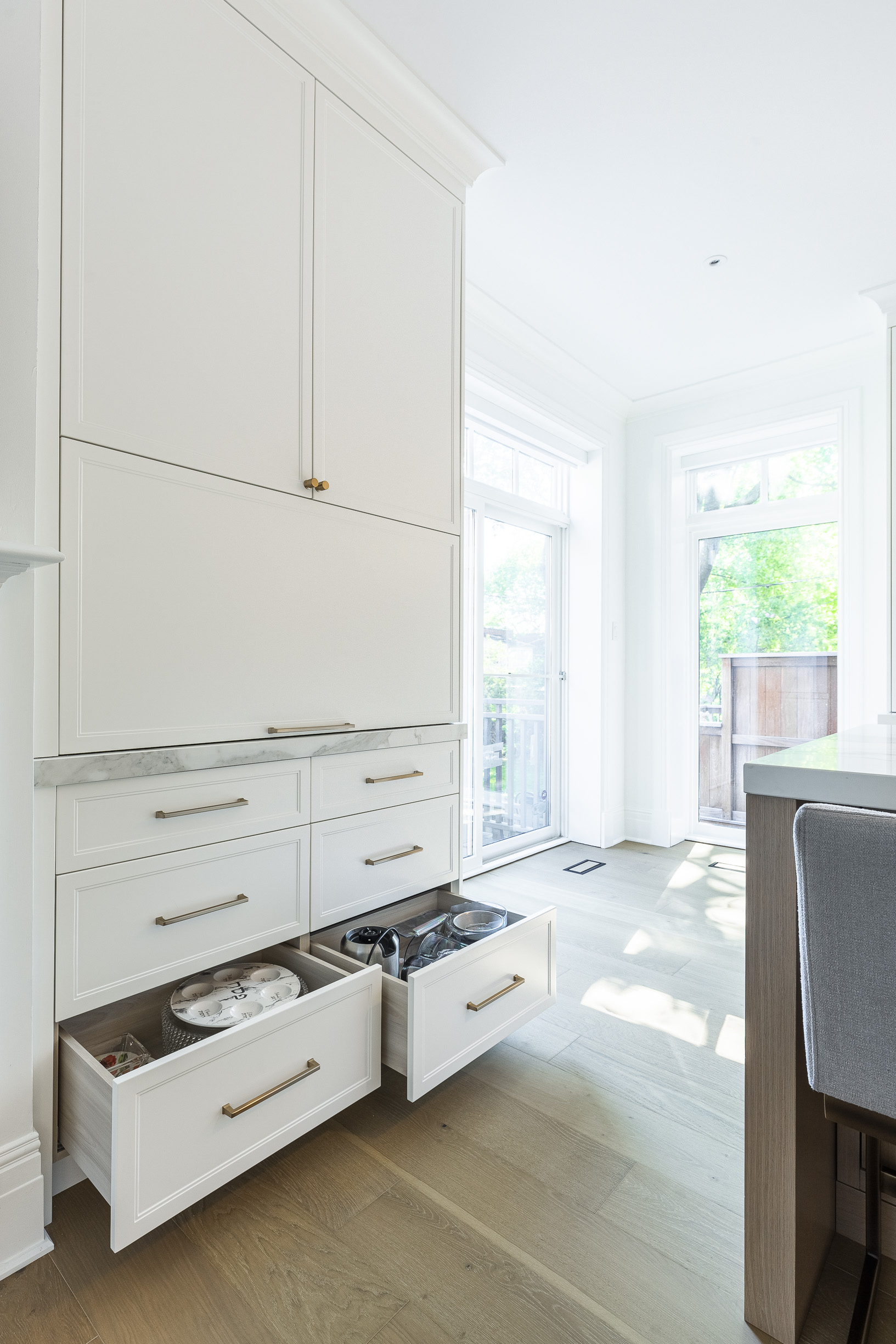 Bright and airy minimalist kitchen corner featuring sleek white cabinetry, brass accents, and natural light for an elegant culinary space.