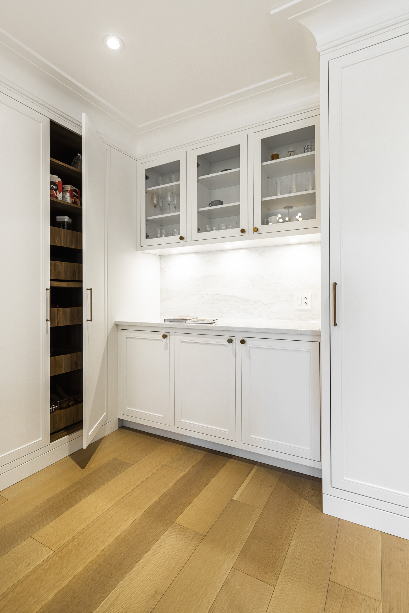 A stylish kitchen corner featuring white cabinetry, a marble countertop, and a chic dark wood pantry for a modern and inviting atmosphere.