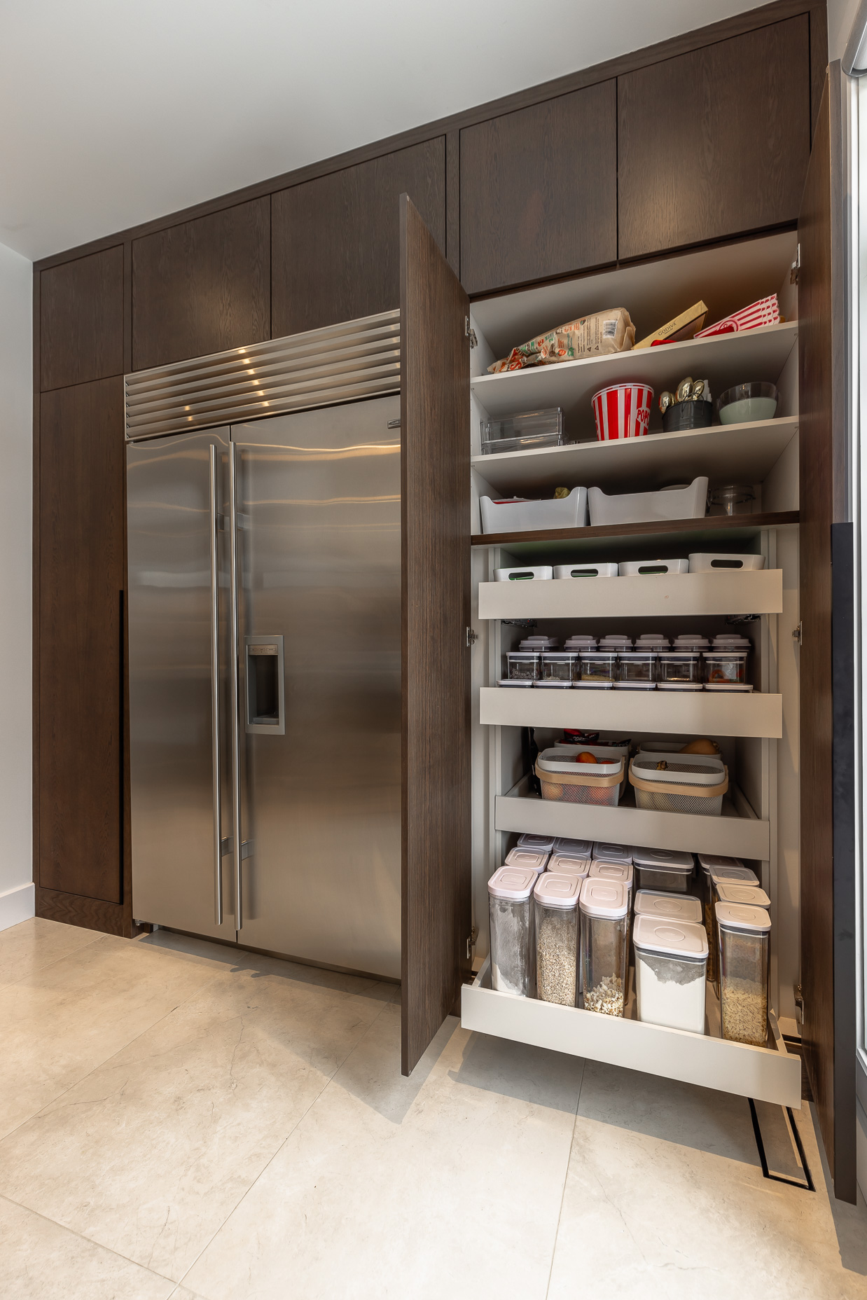 Discover a stylish kitchen corner with a sleek stainless steel fridge and organized pull-out pantry for efficient storage and modern elegance.
