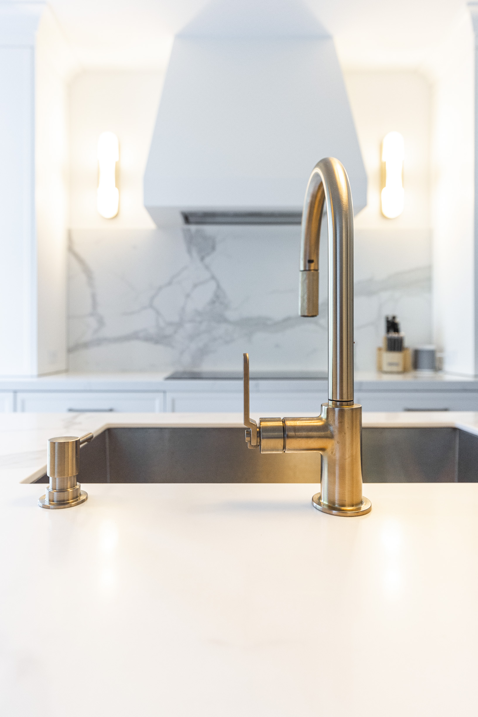 A stunning gold faucet and soap dispenser elevate this modern kitchens elegance against a white countertop and marble backsplash.