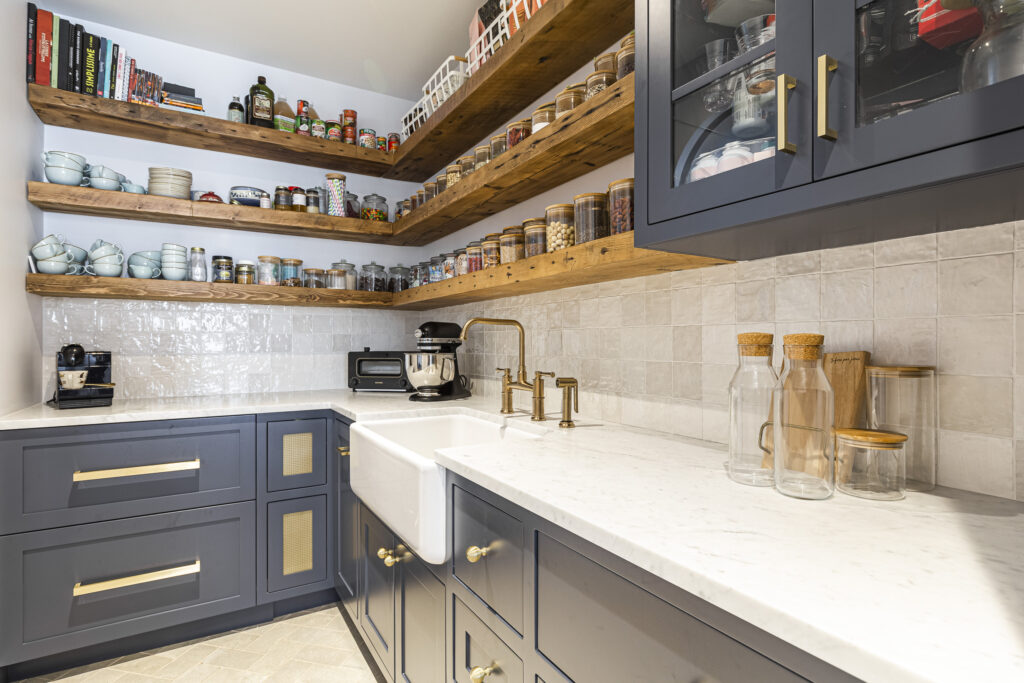 Modern kitchen with navy cabinets, white countertop, rustic shelves, and elegant farmhouse sink.