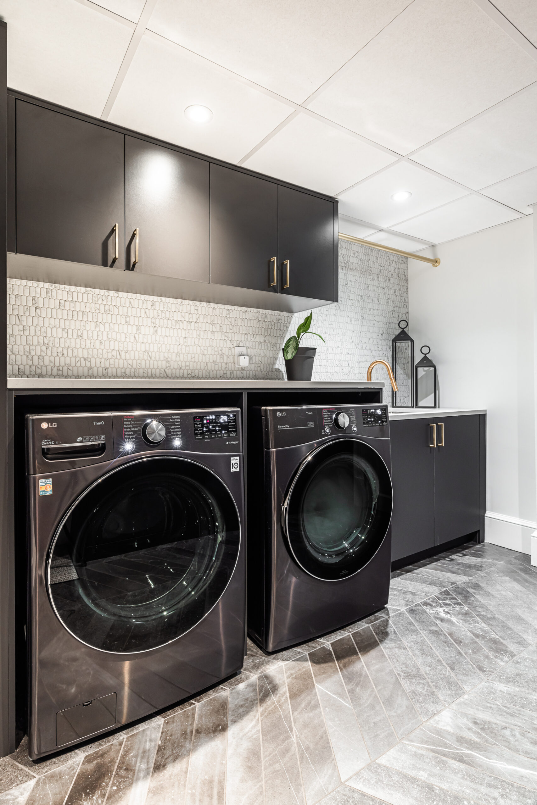 Discover a chic modern laundry room featuring sleek black appliances, stylish cabinetry, and inviting wood-like flooring.