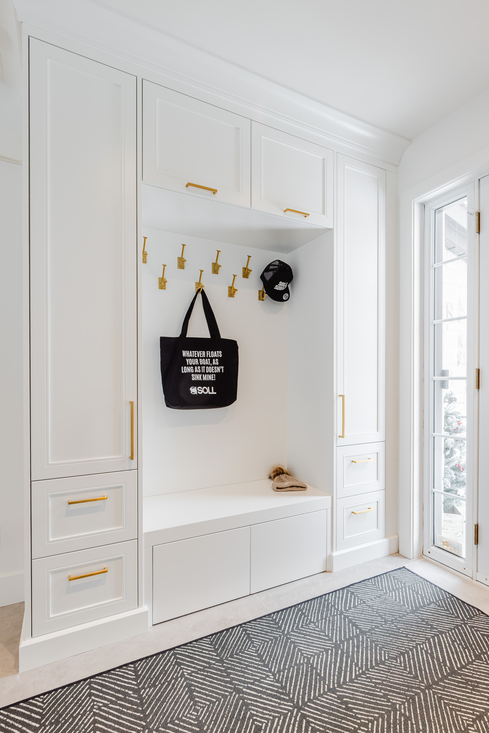 Stunning minimalist entryway featuring white cabinetry, gold accents, and herringbone flooring illuminated by natural light for an inviting feel.