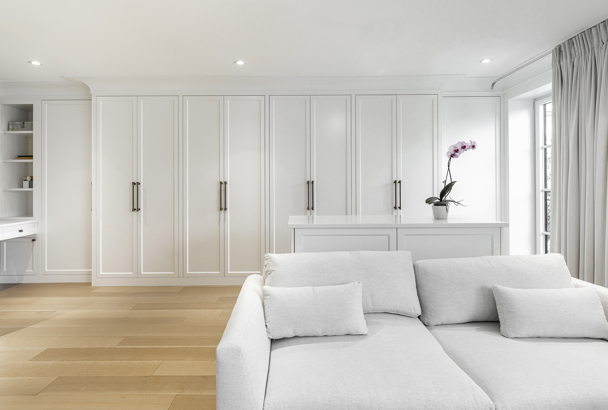 Cozy modern minimalist interior featuring a light gray sofa, sleek cabinets, and a vibrant orchid under bright natural light.