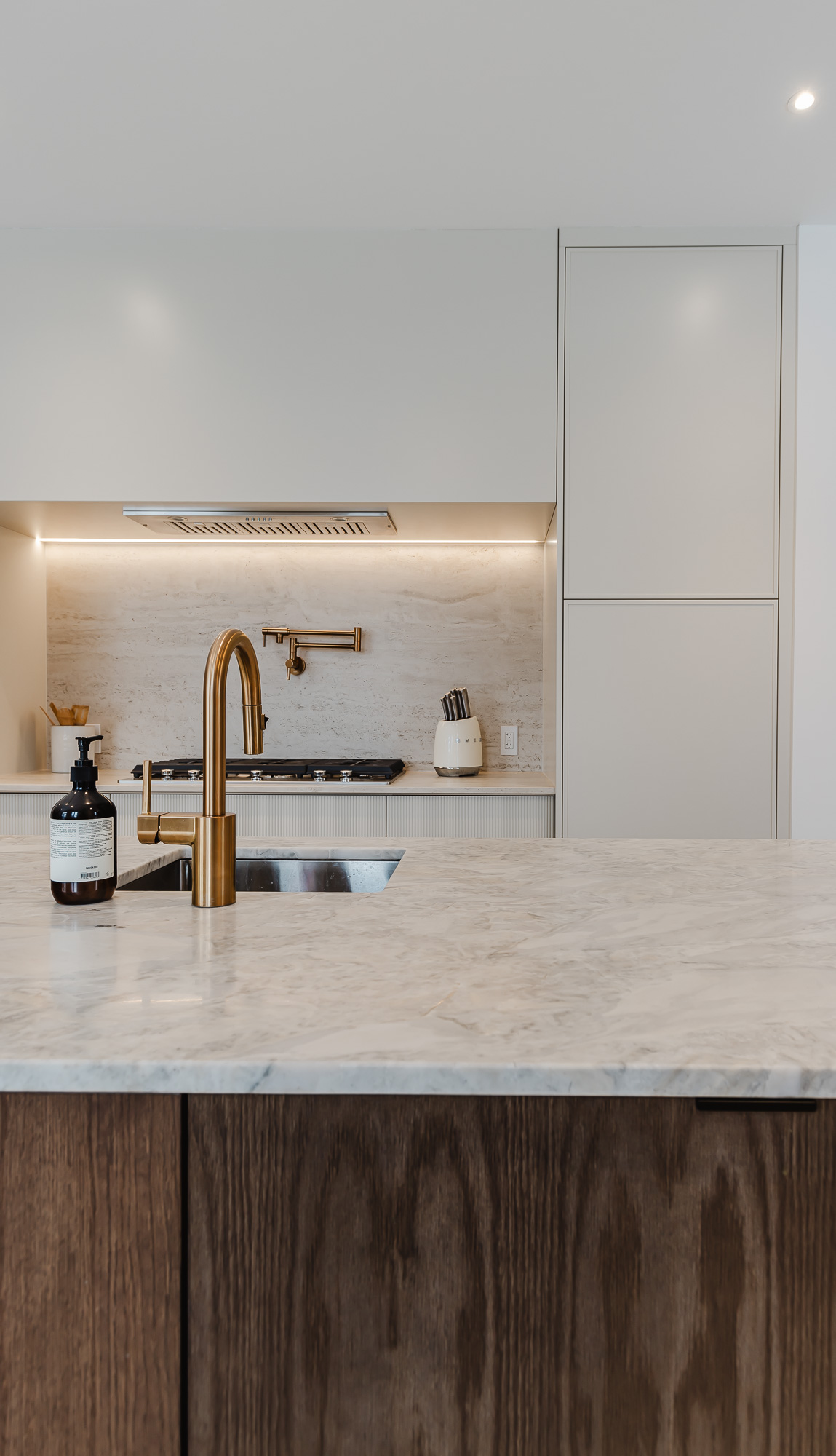 Elevate your home with this elegant modern kitchen featuring light stone countertops, rich wood cabinetry, and stylish matte gold accents.