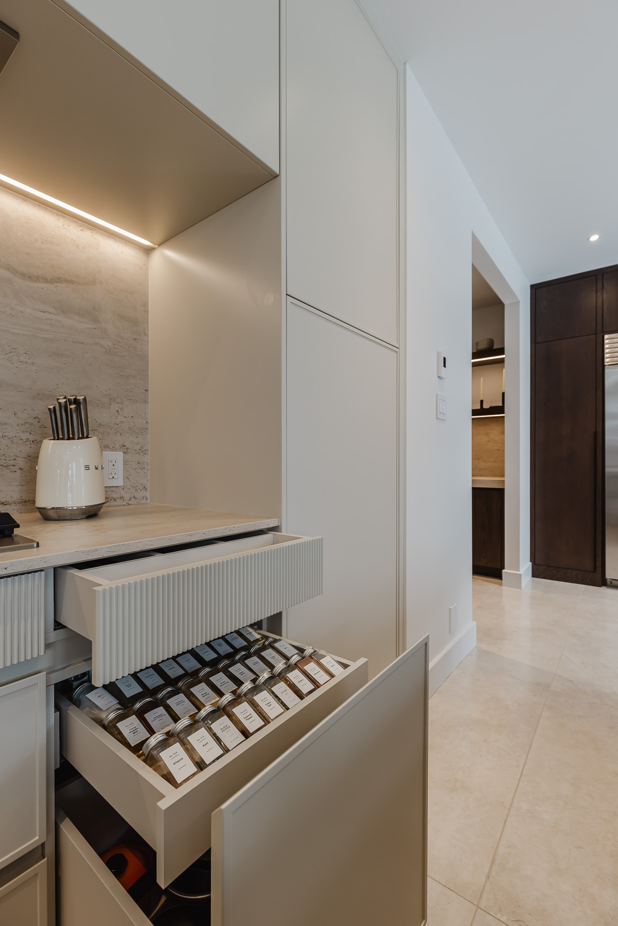 Modern minimalist kitchen featuring light gray cabinetry, a textured stone backsplash, and organized utensils for a stylish and functional space.