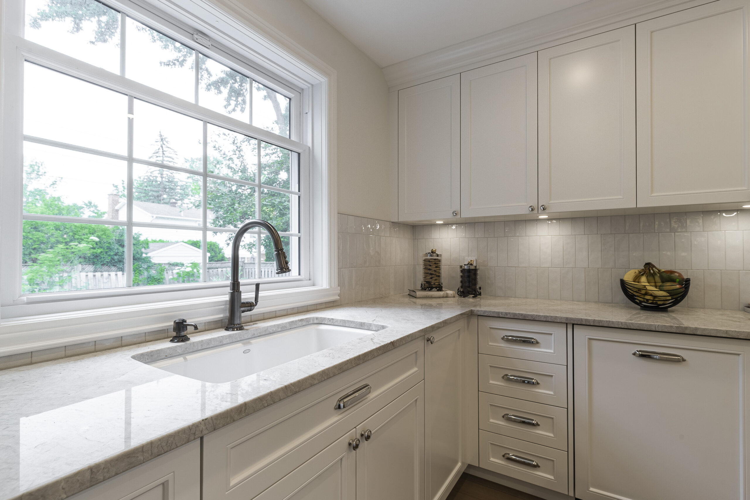 Experience modern elegance in this bright kitchen with white cabinetry, natural light, and a stylish high-arched faucet above a double basin sink.