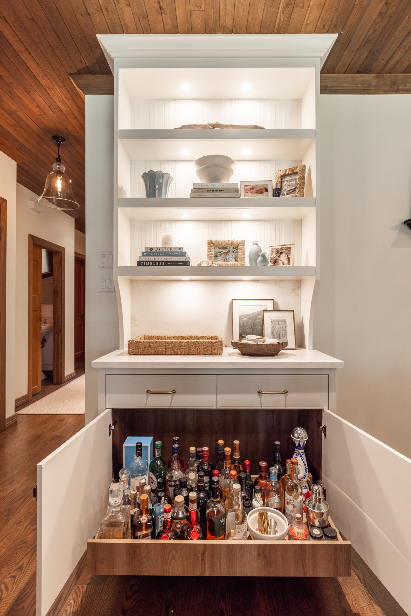 Elegant white storage unit with illuminated shelves and a vibrant mini bar collection, blending style and functionality in a warm, inviting space.