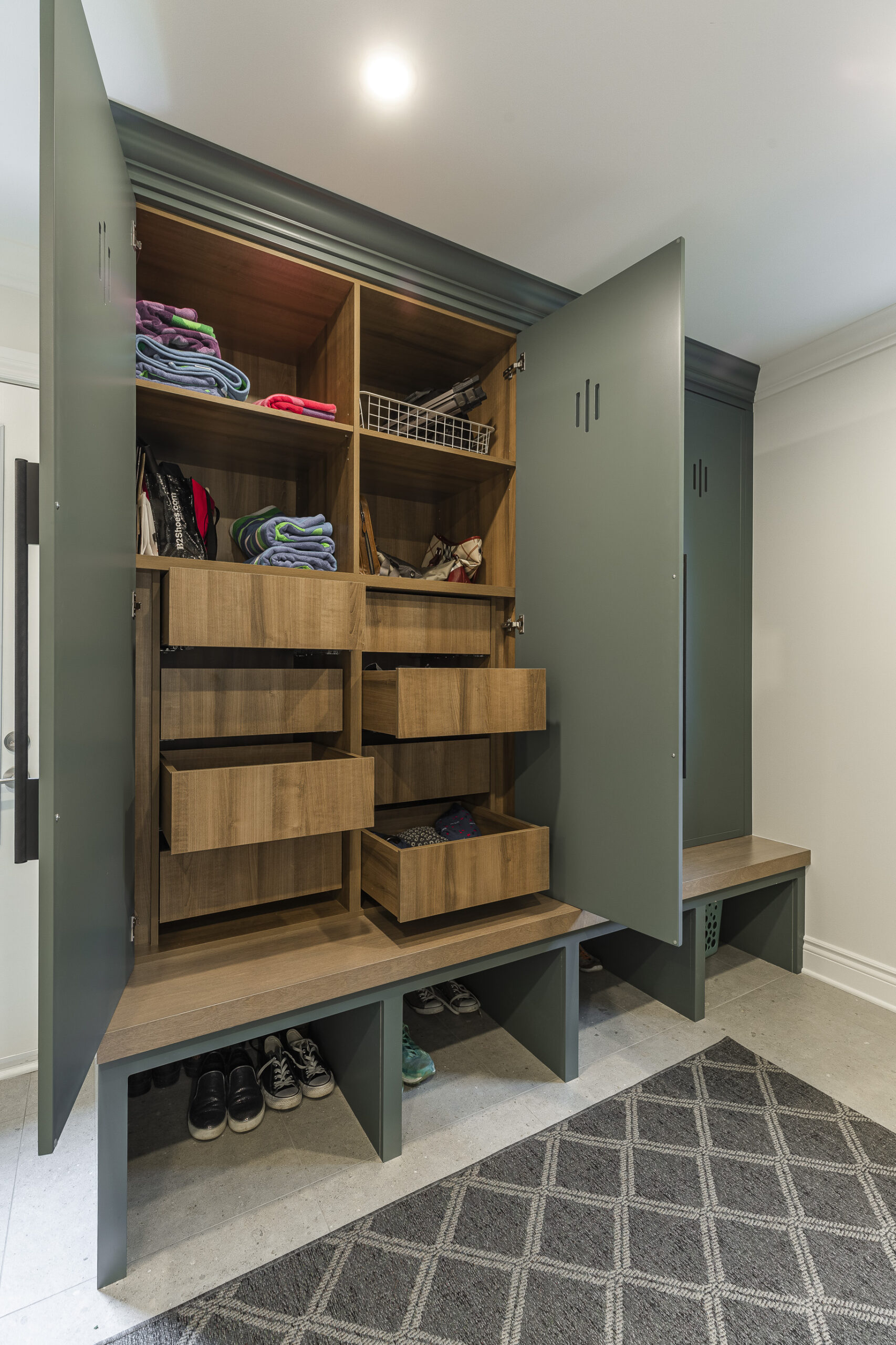 Stylish mudroom cabinet in muted green features ample storage, rustic drawers, and built-in benches for a functional and inviting entryway.