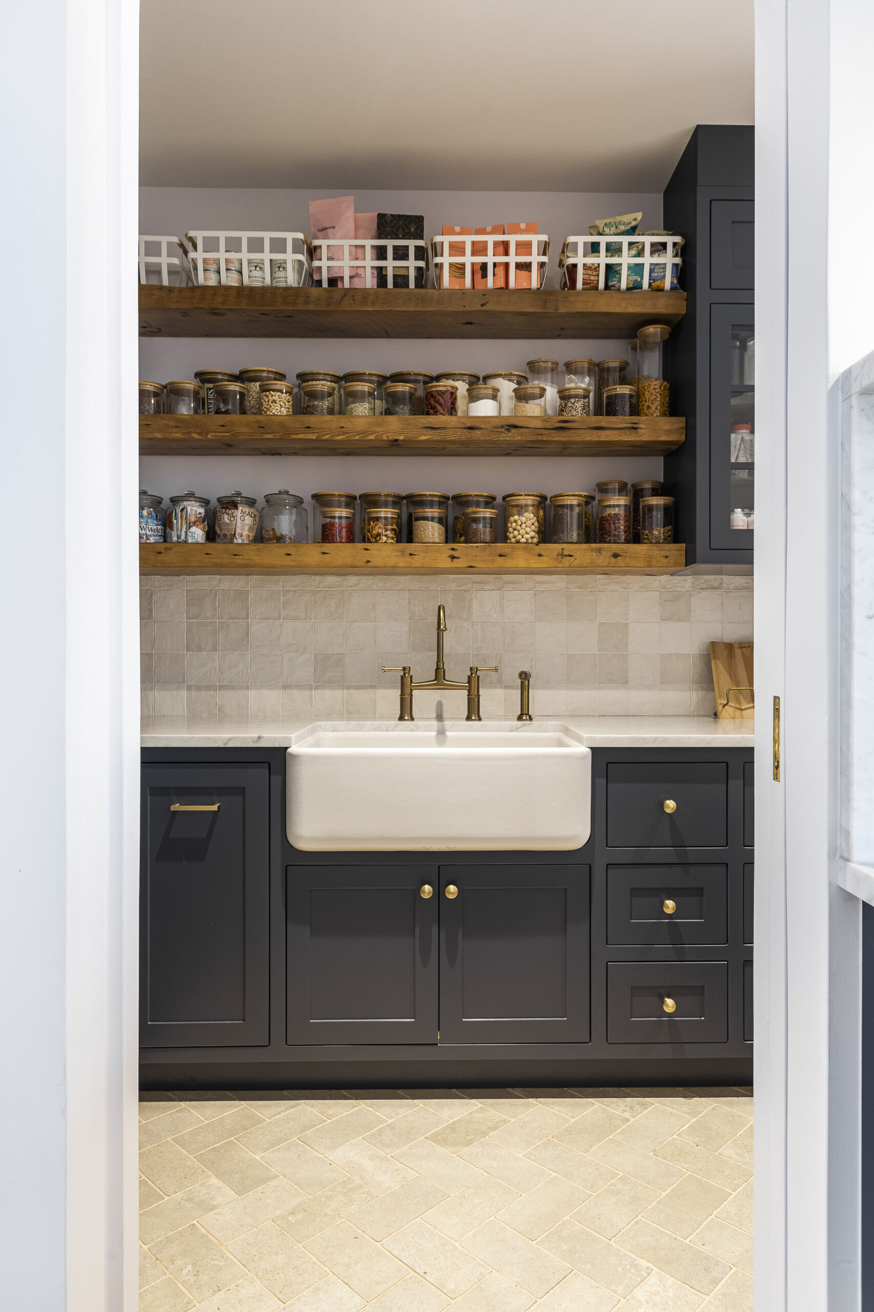 This modern gray pantry features elegant wood accents, organized shelving, and a stylish farmhouse sink, creating a warm and inviting atmosphere.