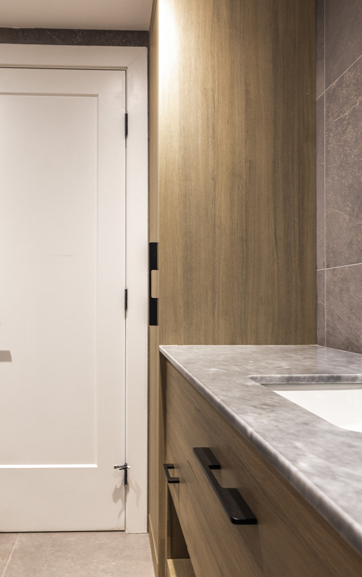 Discover a serene minimalist bathroom blending warm wood, light gray stone, and textured tiles for a stylish and functional design.