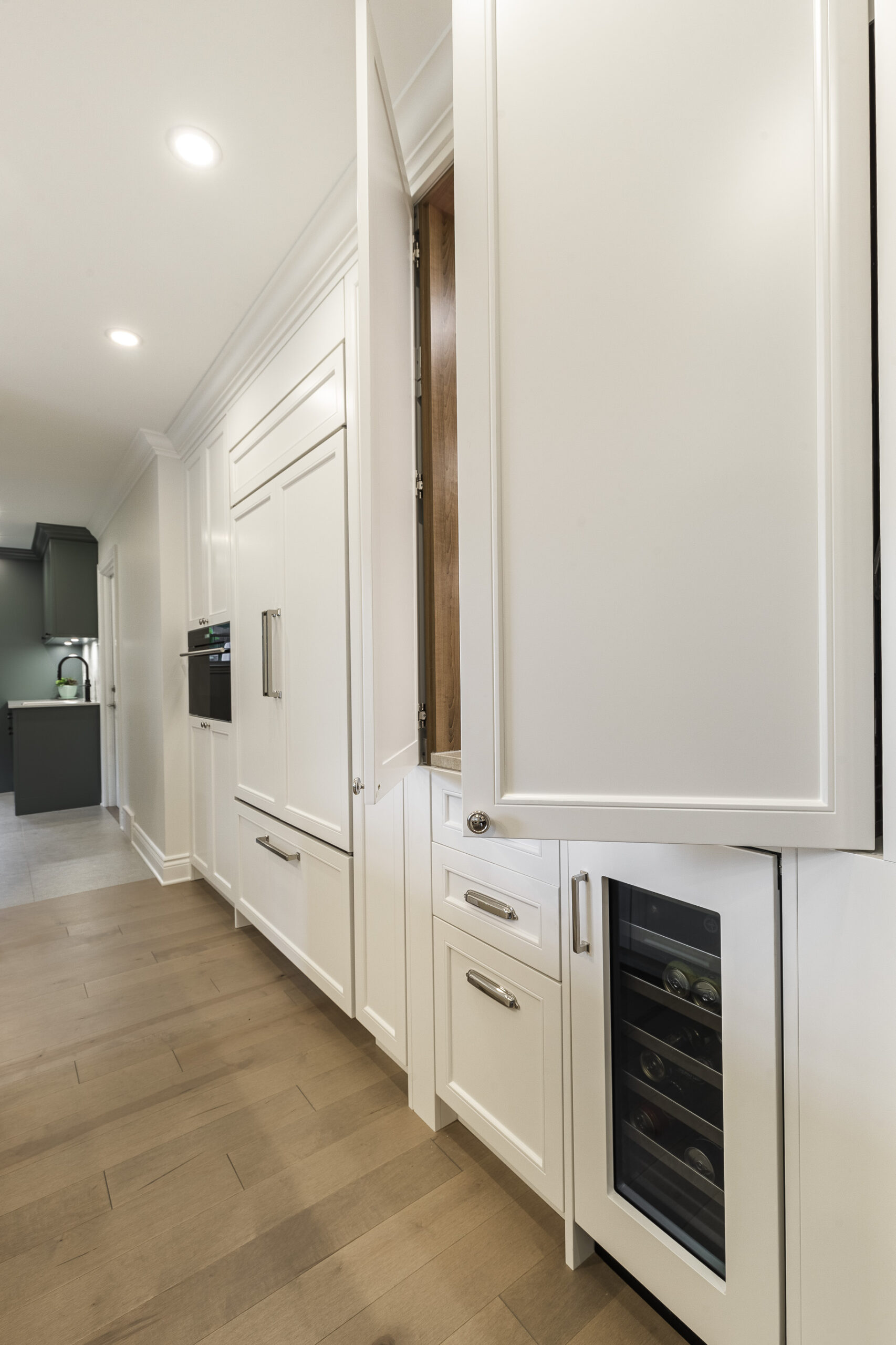 Discover a stylish modern kitchen featuring sleek white cabinetry, a wine cooler, and warm light hardwood flooring for a welcoming atmosphere.