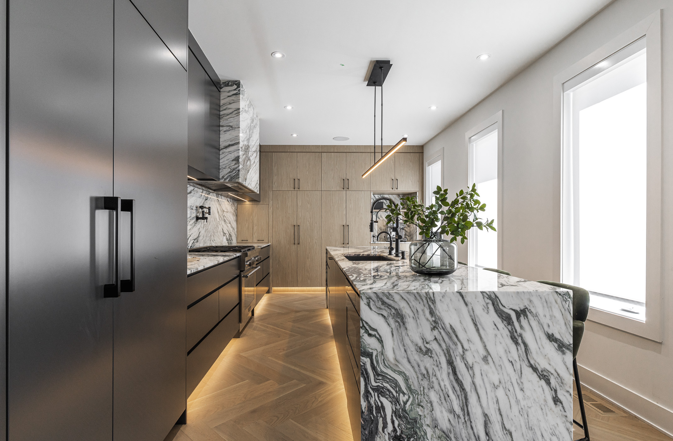 Elegant minimalist kitchen featuring contrasting black and wood cabinetry, a luxurious marble island, and abundant natural light.
