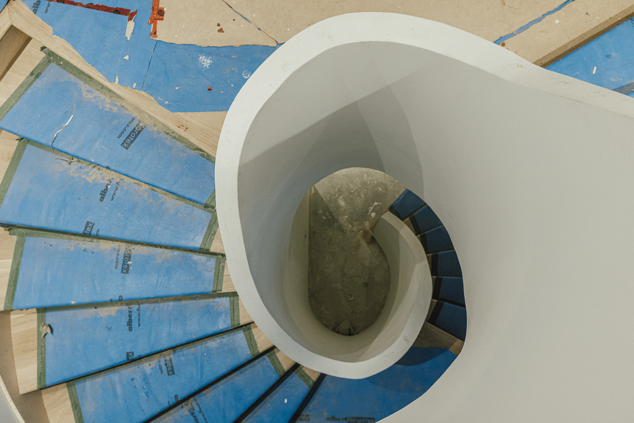 A sleek modern spiral staircase under construction, featuring wide protective treads and elegant white walls.