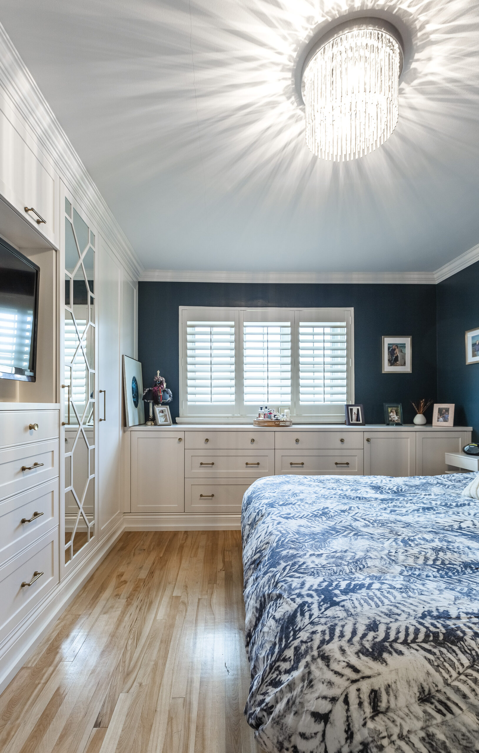 Modern bedroom with deep blue walls, elegant chandelier, and a cozy atmosphere, perfect for relaxation and stylish living.