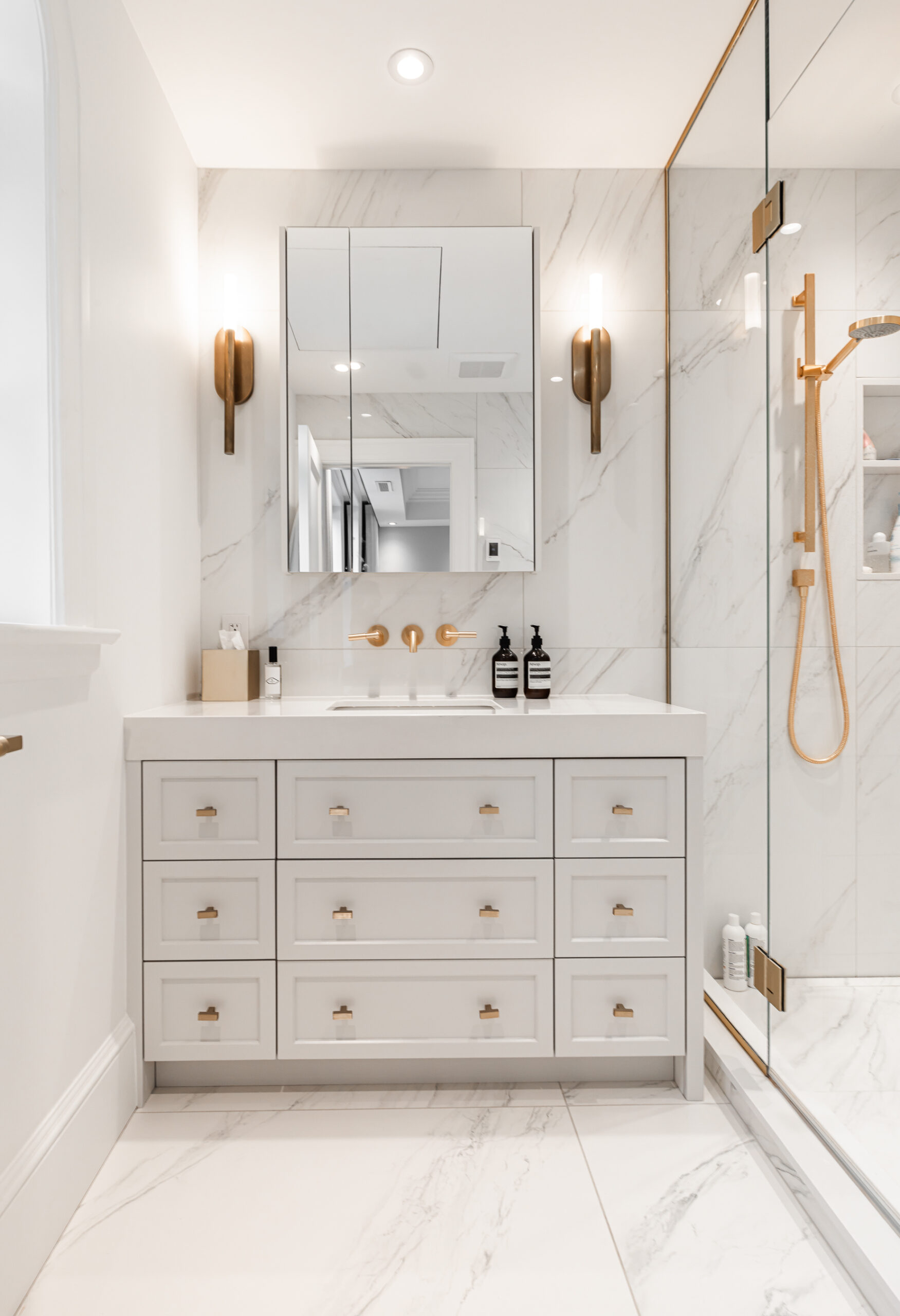 Discover a serene modern bathroom featuring a white vanity, brass accents, and a stylish walk-in shower with marble finishes.