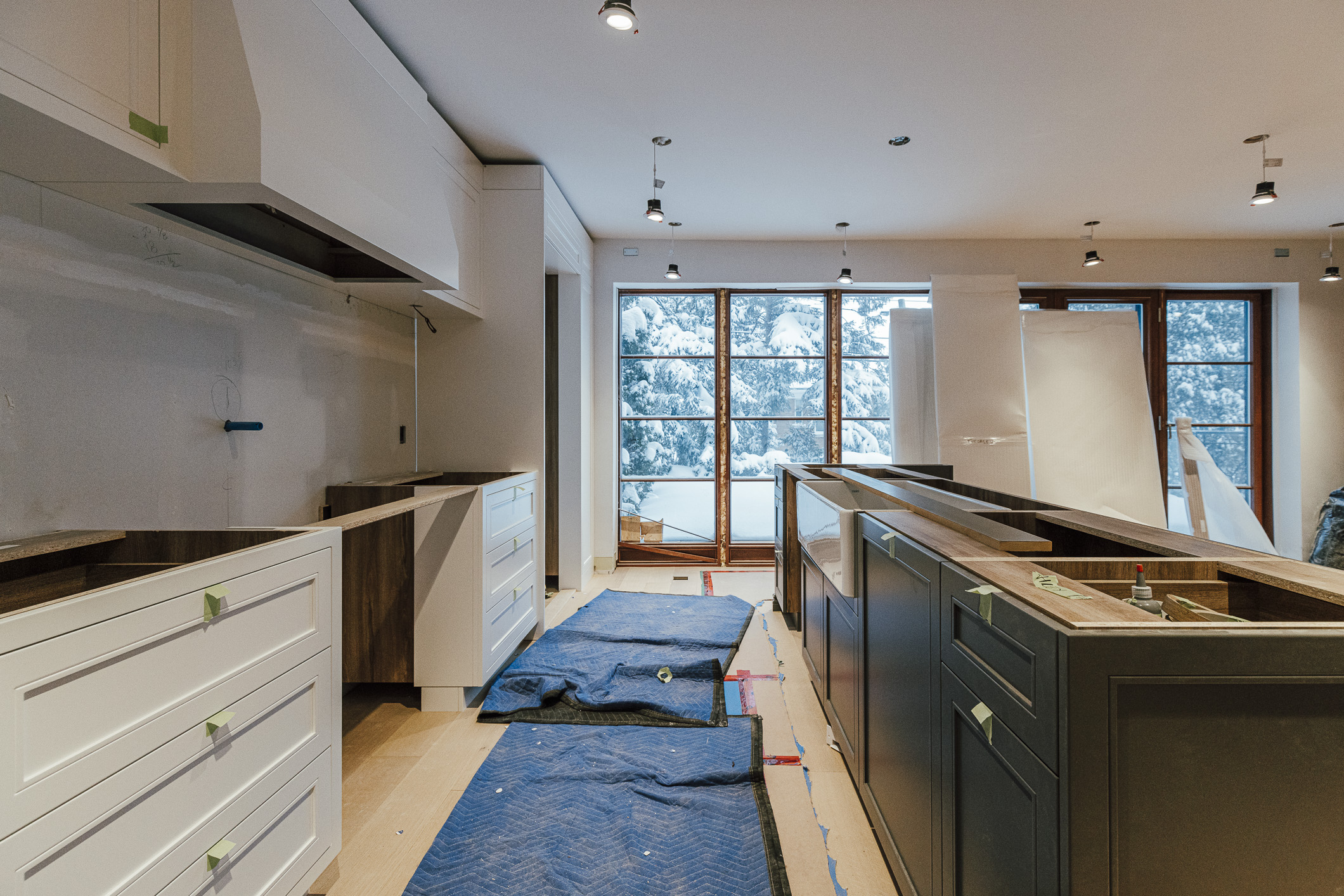 A modern kitchen renovation showcases contrasting cabinets and large windows, promising a bright and inviting space once completed.