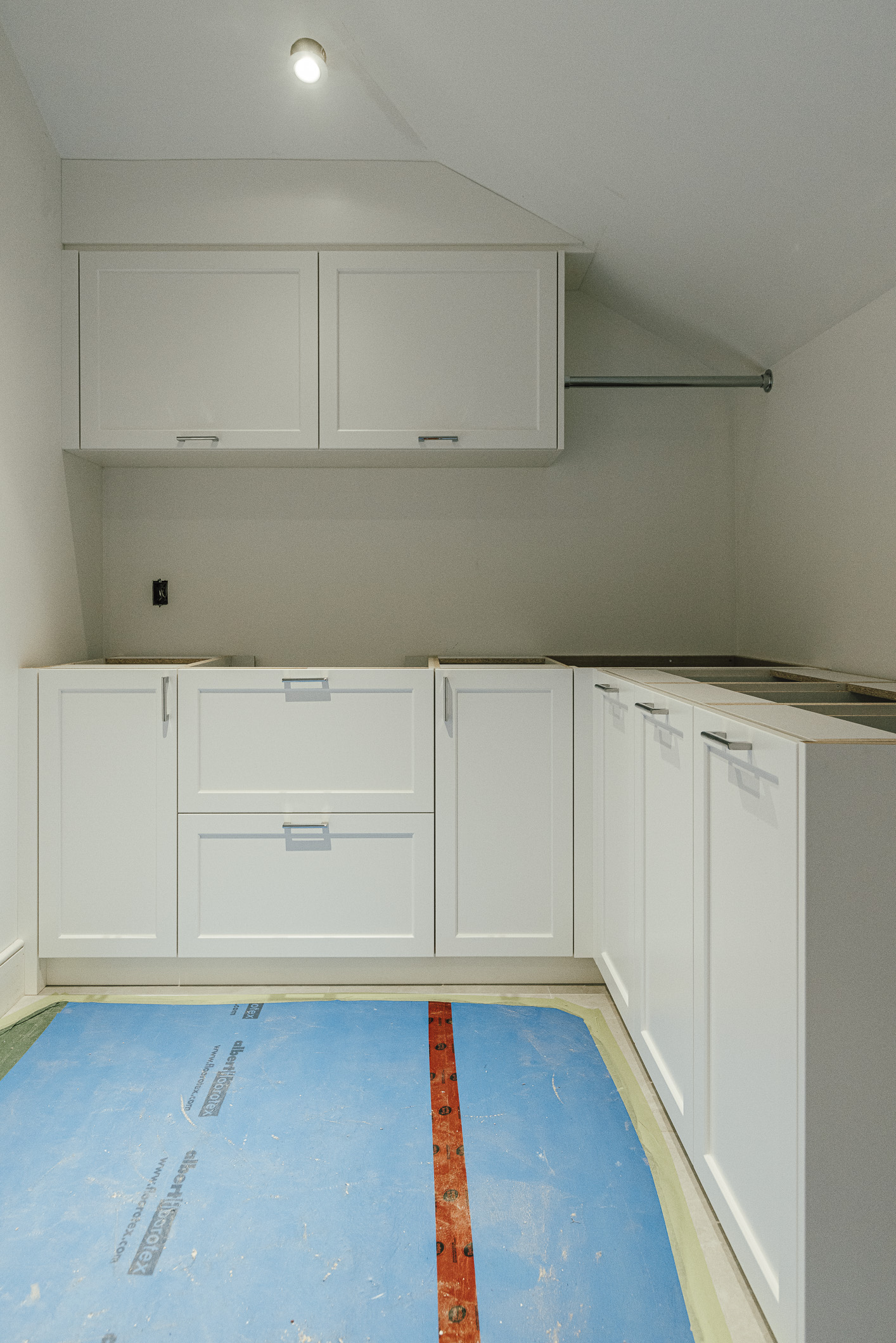 A sleek, modern utility room featuring white cabinets is currently undergoing renovations, showcasing an unfinished countertop and protective flooring.