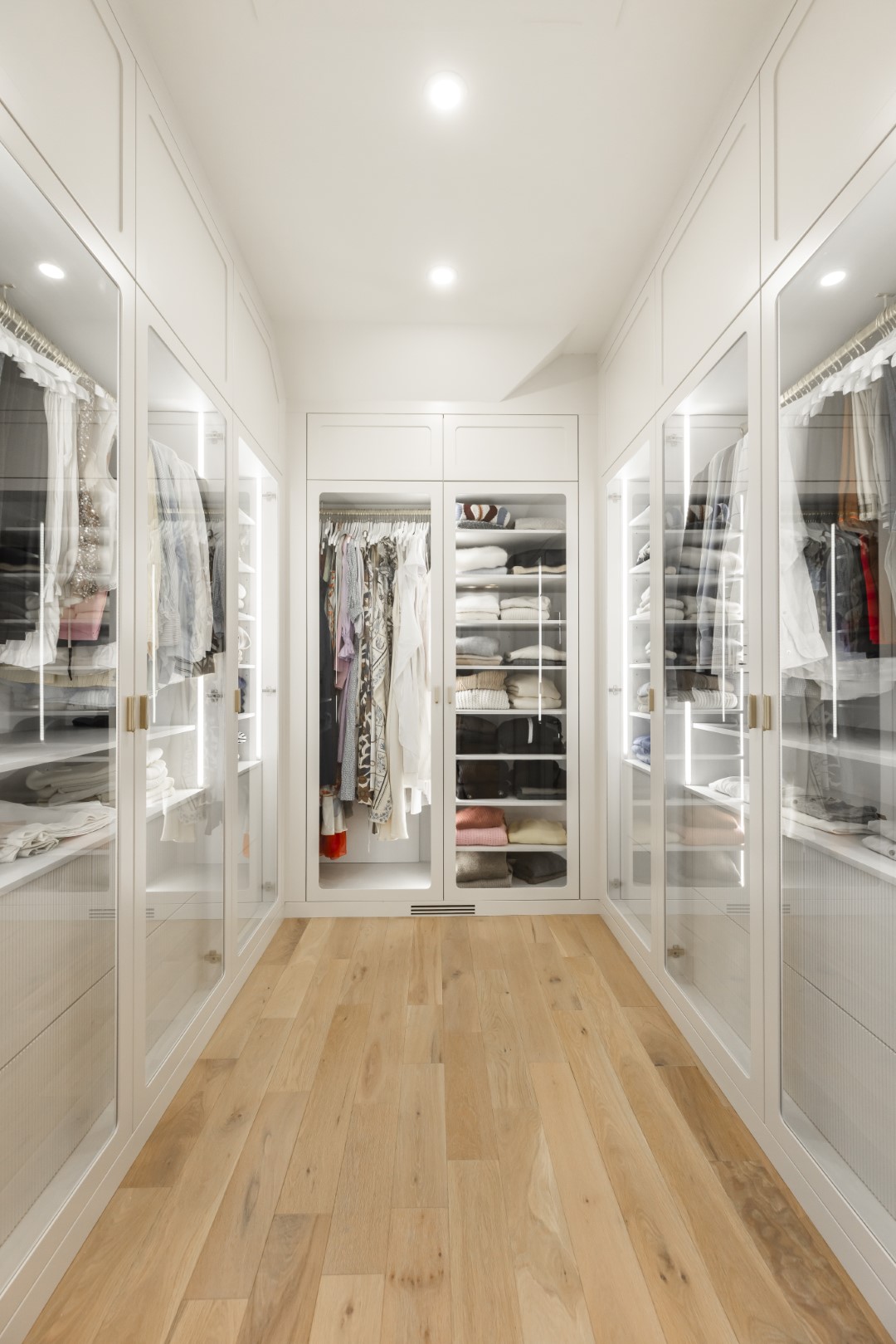 Discover an elegant walk-in closet with glass-front cabinetry, showcasing organized fashion and a warm, inviting ambiance.