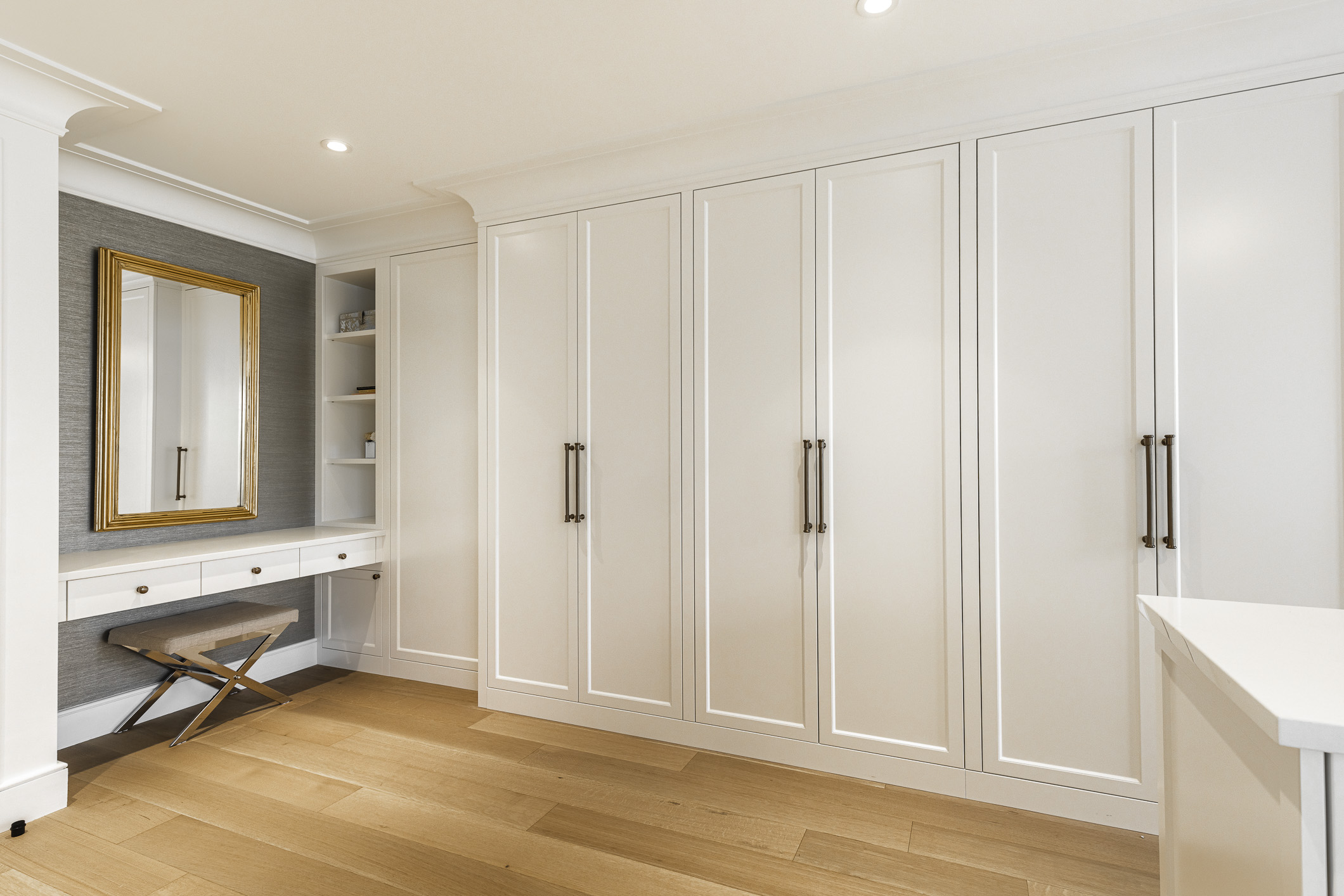 Discover a chic walk-in closet with glossy cabinetry, a stylish vanity, and warm wooden flooring for an elegant daily routine space.