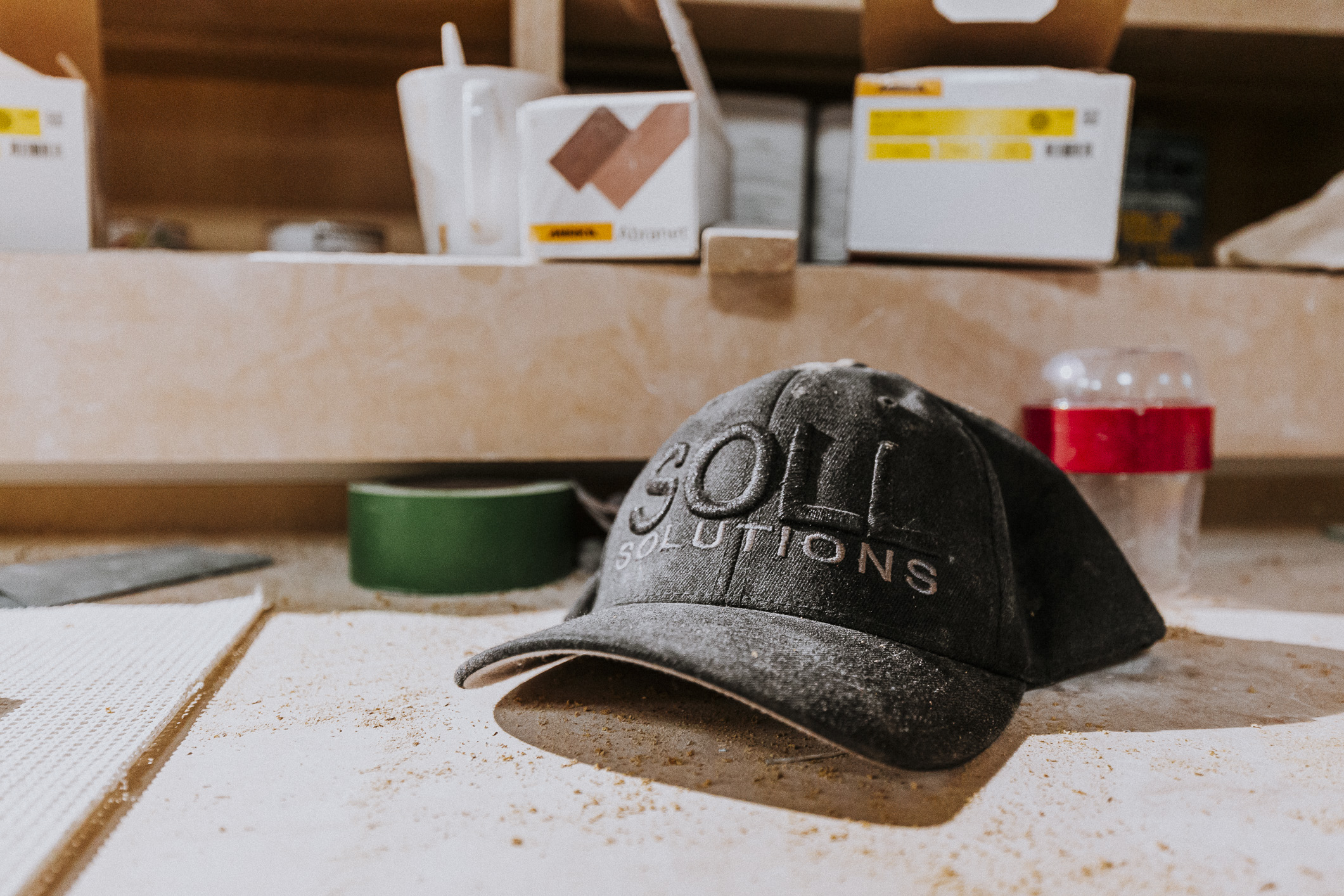 A well-worn cap labeled SOLUTIONS rests in a dynamic workspace, exemplifying craftsmanship amid tools and materials.