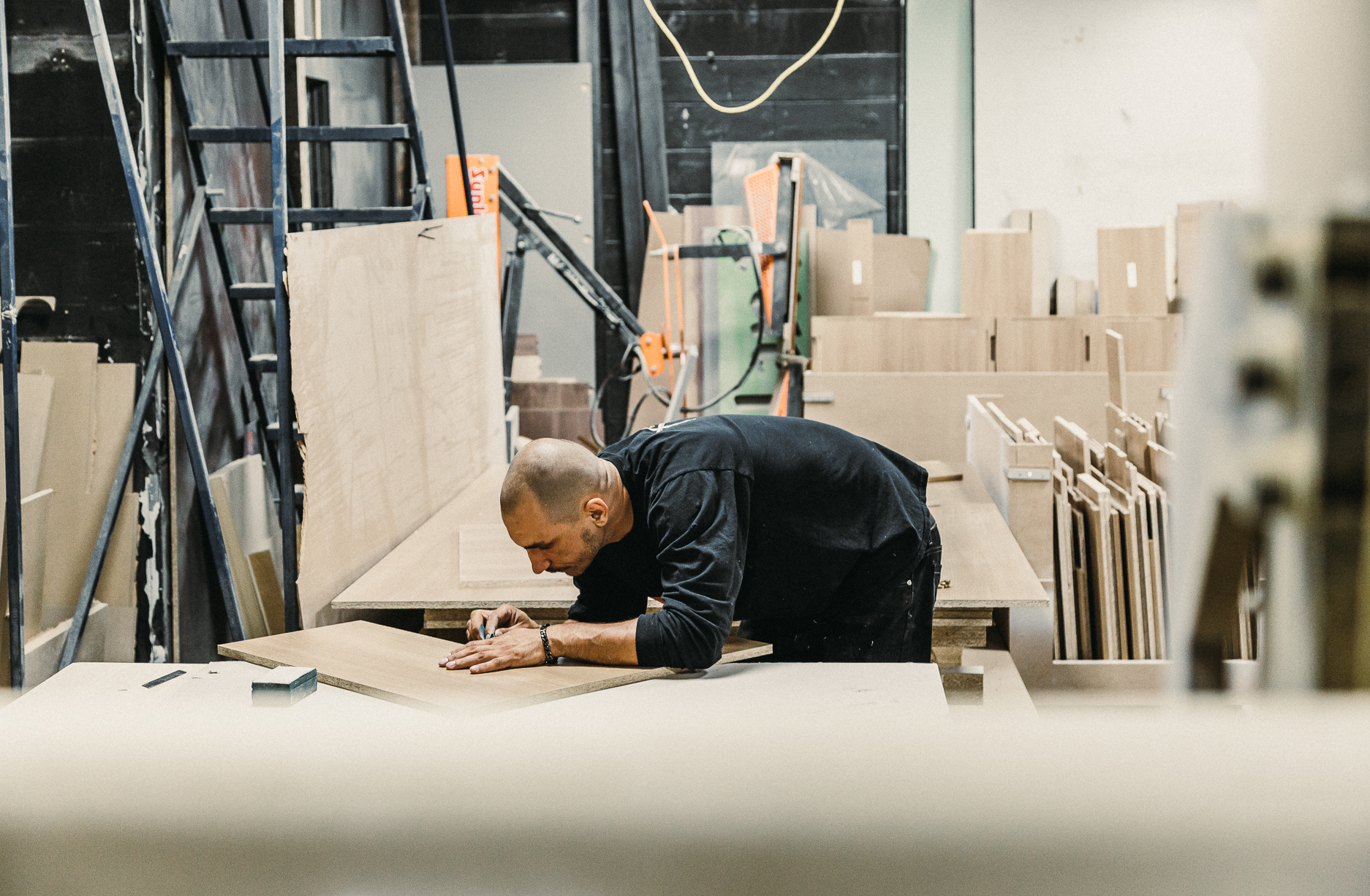 A dedicated carpenter measures wood in a spacious workshop, showcasing his craftsmanship amidst tools and raw materials.