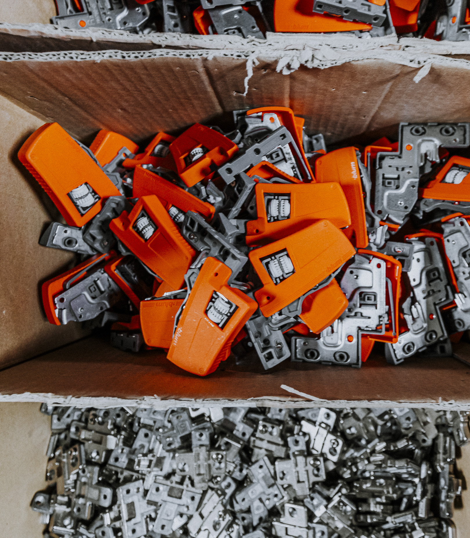 A well-organized box displays vibrant orange clips alongside metallic hinges, showcasing efficient hardware storage and contrast in design.