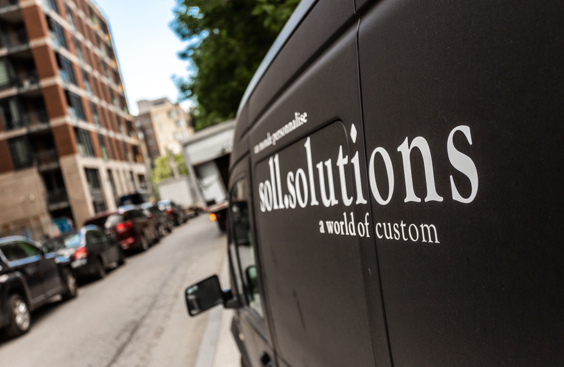 A sleek black van branded soul.solutions is parked on a bustling city street, showcasing custom services amid vibrant urban life.