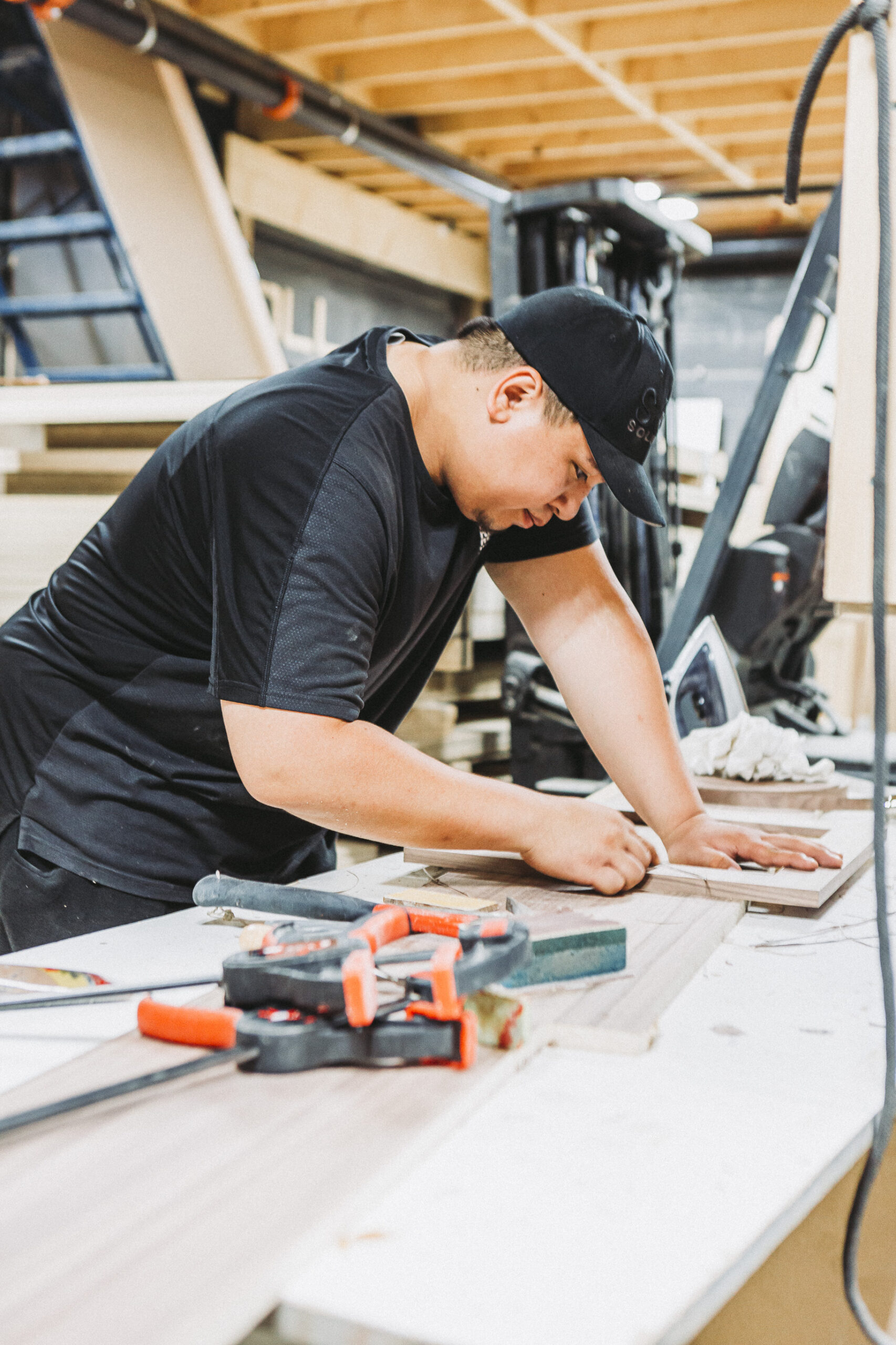 A focused woodworker meticulously measures and sketches on wood in a vibrant, tool-filled workshop.