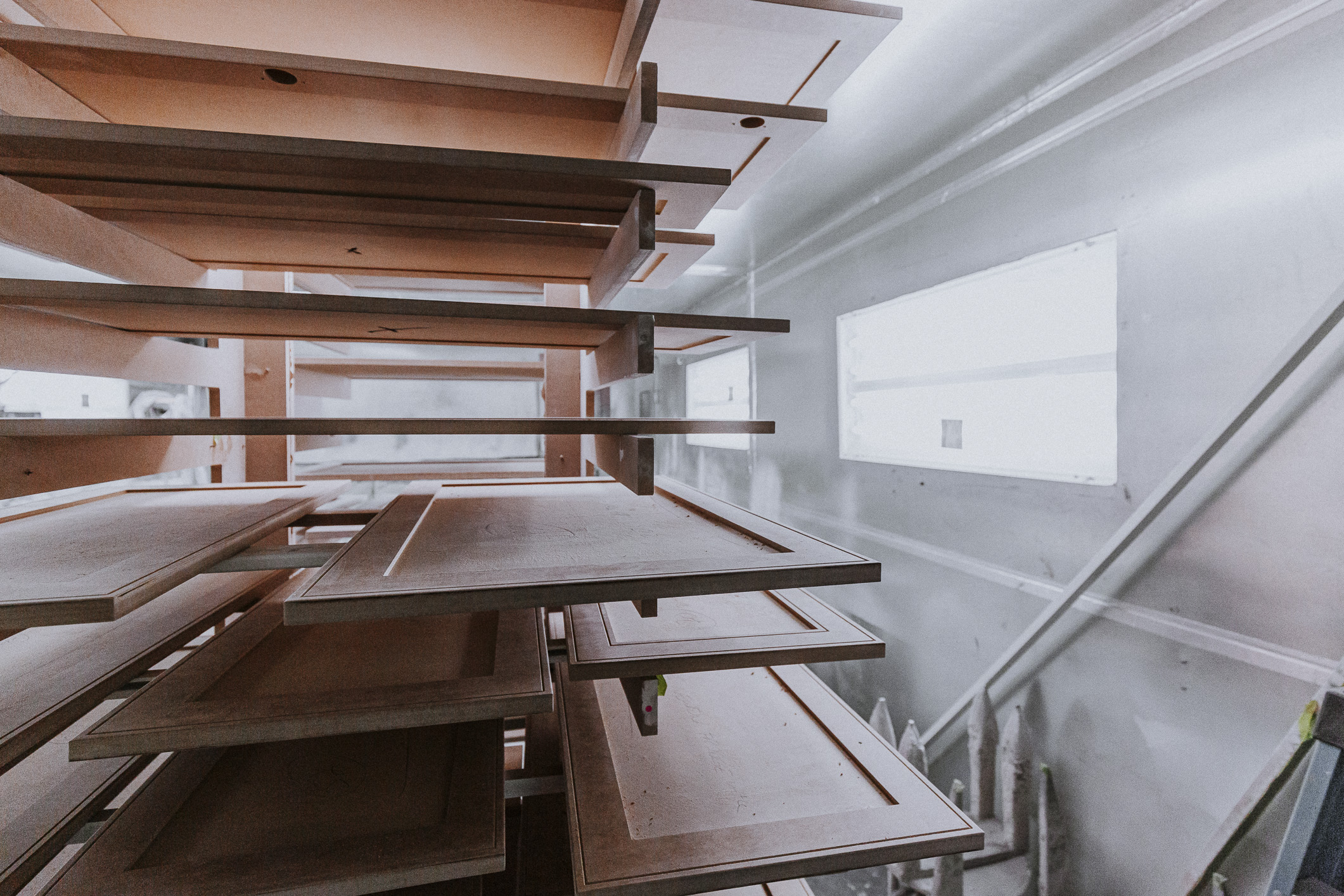 Sunlight streams through a window, illuminating neatly stacked wooden panels in a modern, organized woodworking workshop.