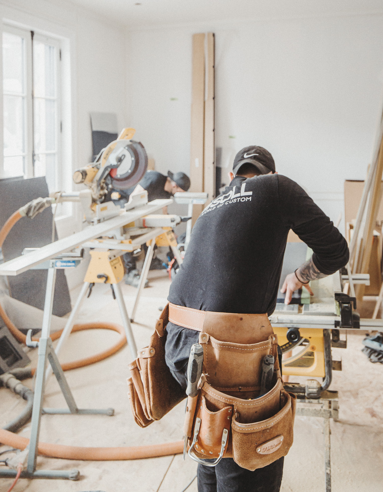 A focused carpenter operates a table saw in a vibrant woodworking workshop, emphasizing teamwork and craftsmanship in natural light.