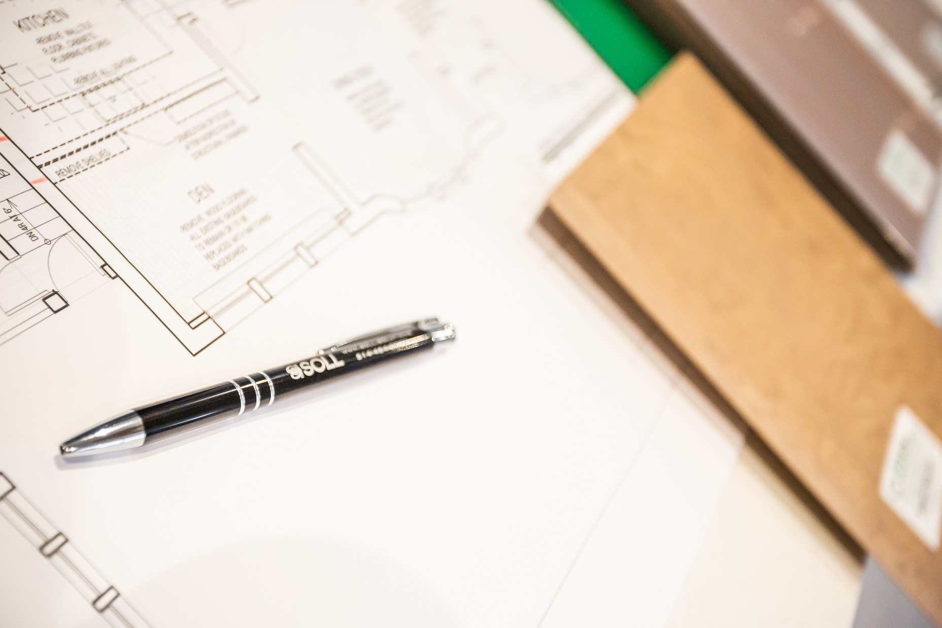 Detailed architectural plans on a workspace, paired with a sleek pen and material samples, showcase the design and planning process.